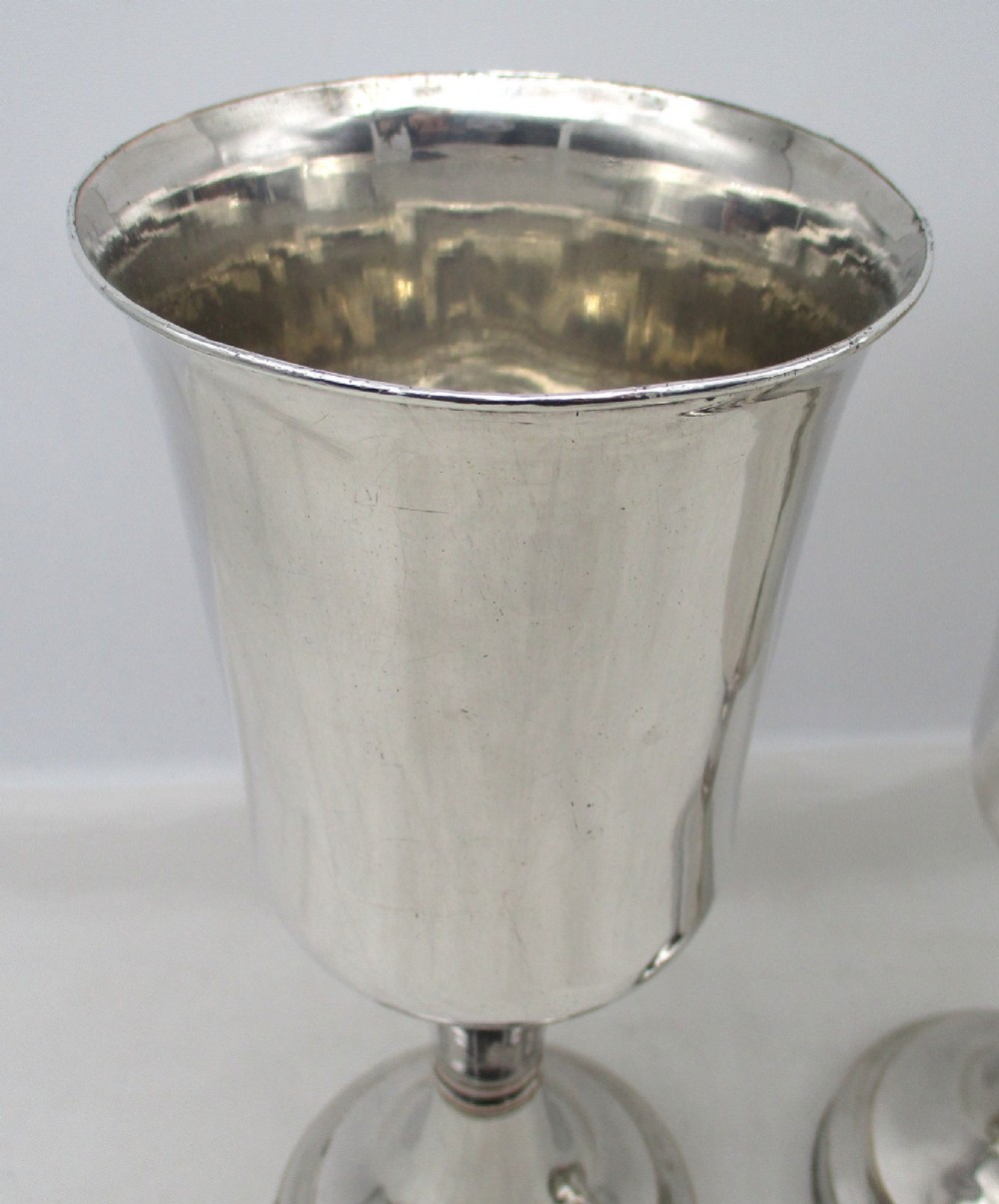A pair of tall silver-plated church chalices featuring flared rims, knopped central stems, and stepped circular bases. View II