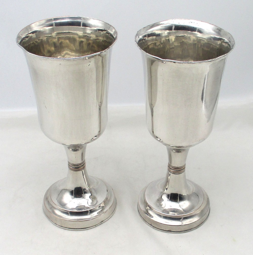 A pair of tall silver-plated church chalices featuring flared rims, knopped central stems, and stepped circular bases. View V