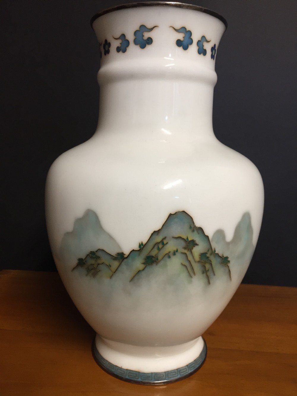 A white Japanese cloisonne enamel vase depicting a green and blue landscape with mountains, pagodas, and trees, finished with a silver rim. View IV