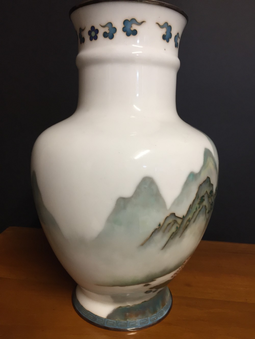 A white Japanese cloisonne enamel vase depicting a green and blue landscape with mountains, pagodas, and trees, finished with a silver rim. View V