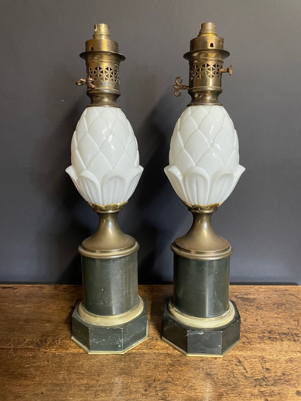 A pair of brass table lamps featuring moulded white glass pineapple bodies set upon dark octagonal marble bases.