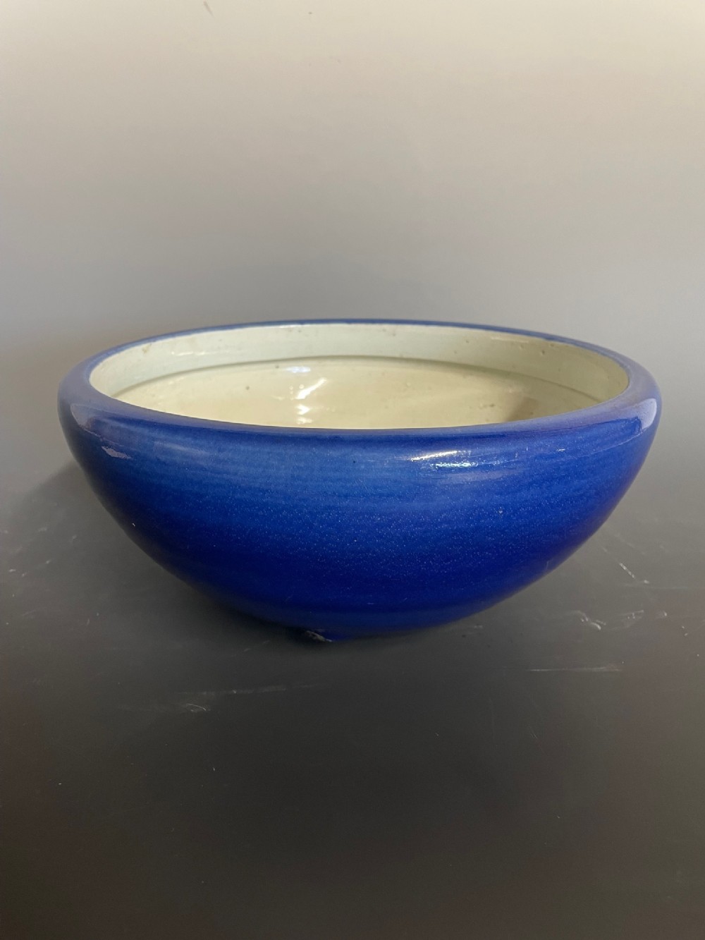 A rounded ceramic bowl featuring a deep cobalt blue glazed exterior and a pale off-white interior.