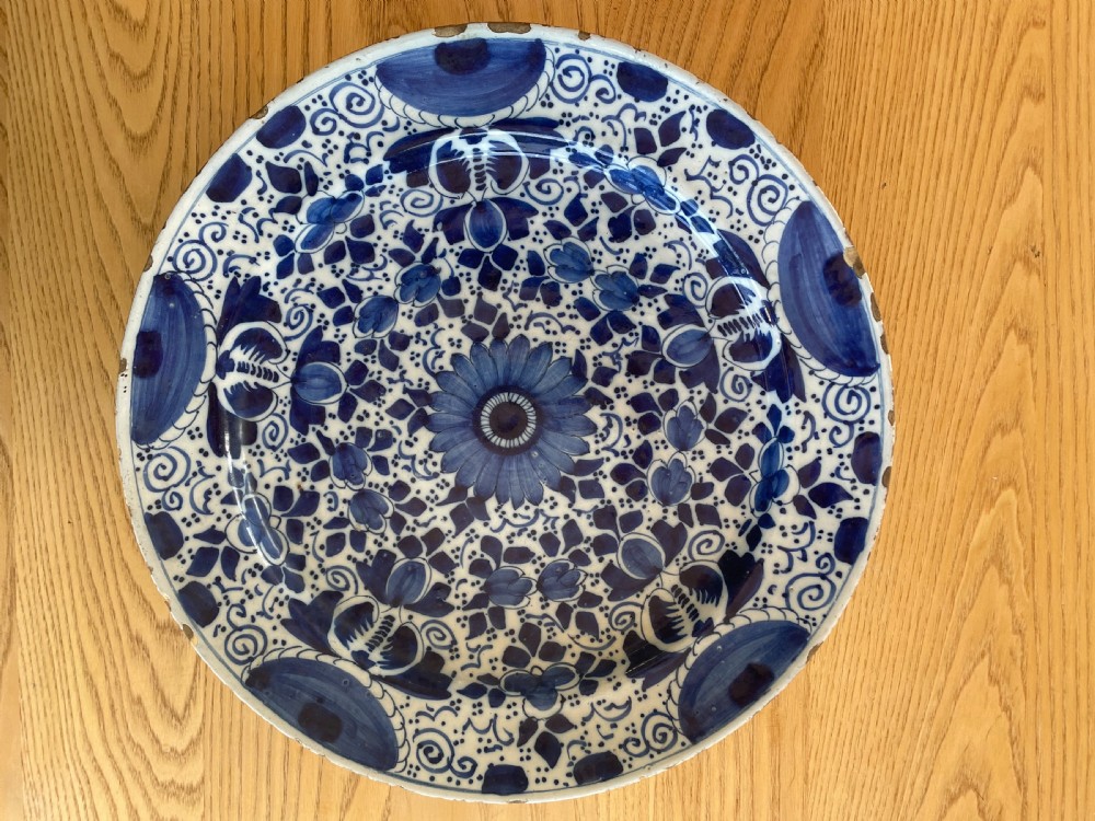A circular tin-glazed earthenware charger featuring hand-painted cobalt blue floral and geometric motifs across its surface with minor glaze loss along the rim.
