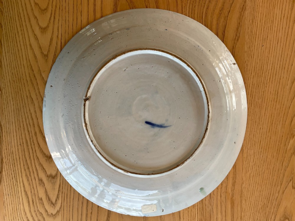 A circular tin-glazed earthenware charger featuring hand-painted cobalt blue floral and geometric motifs across its surface with minor glaze loss along the rim. View II