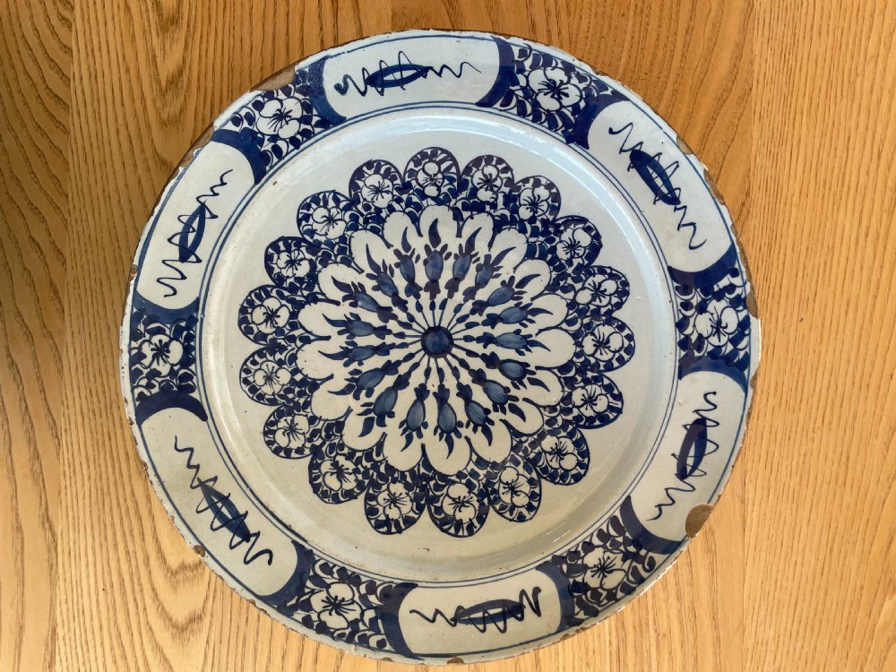 An antique circular Dutch Delft tin-glazed earthenware charger decorated with cobalt blue floral patterns and a central rosette motif against a white glaze.