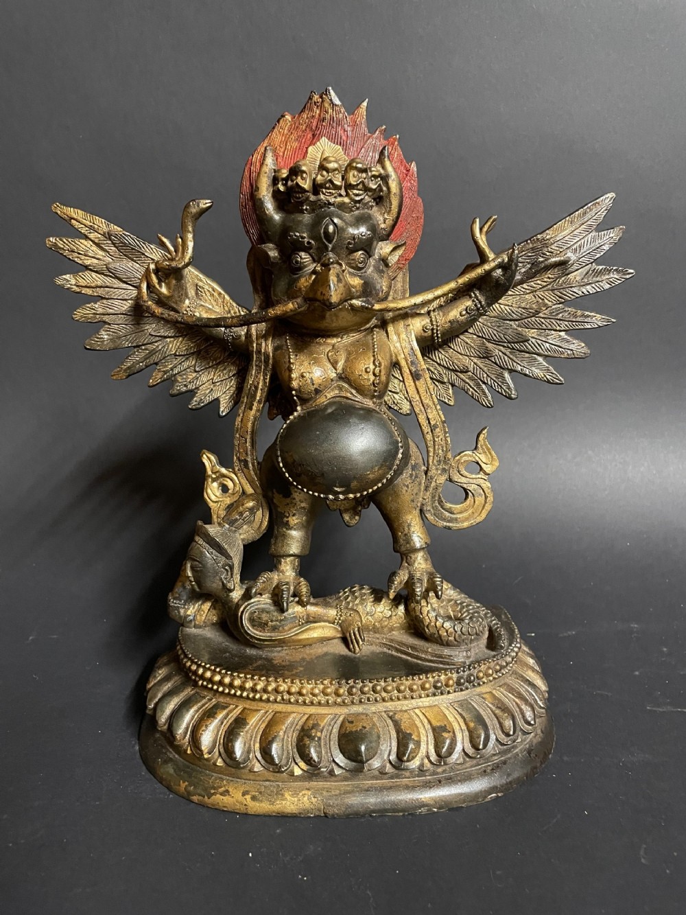 A cast bronze figure of the winged deity Garuda standing upon a double-lotus base with raised arms and outstretched wings.