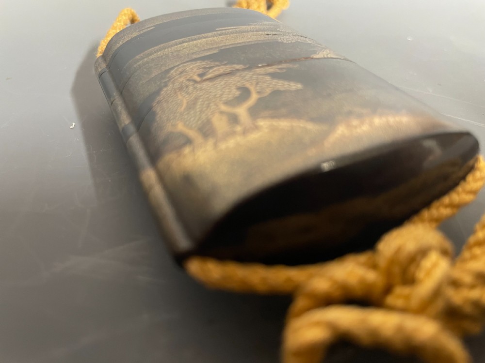 A small Japanese multi-tiered black lacquer inro box decorated with gold maki-e landscape imagery and suspended by a woven yellow cord. View IV