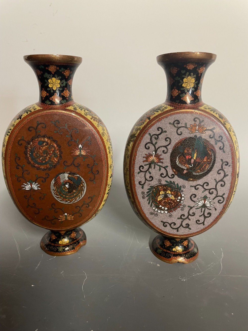 A pair of Japanese cloisonne enamel moon-flask vases featuring dragon medallions and floral scrollwork on flared bases.