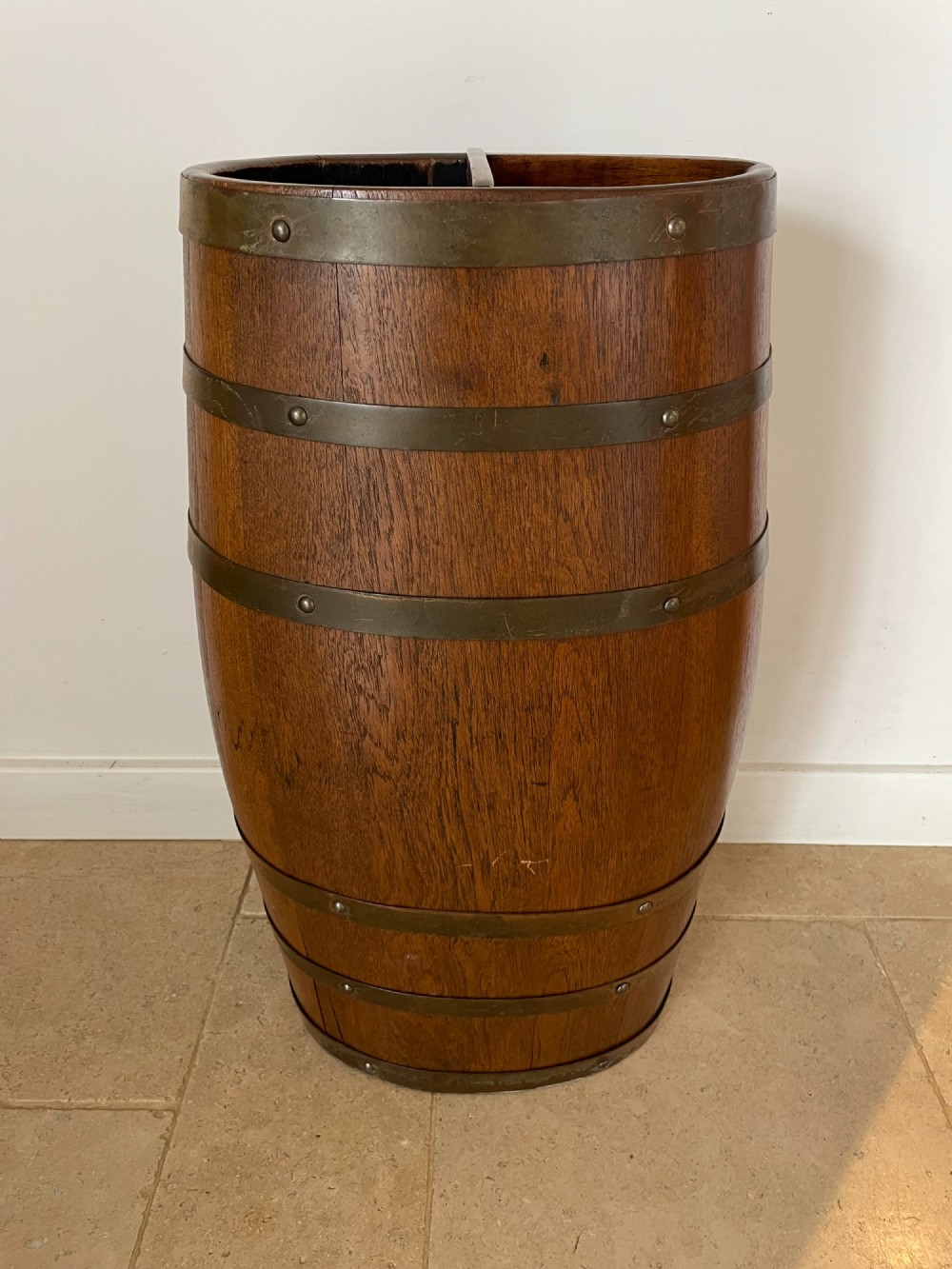 A barrel-shaped coopered oak umbrella stand featuring riveted metal bands and a central top divider.