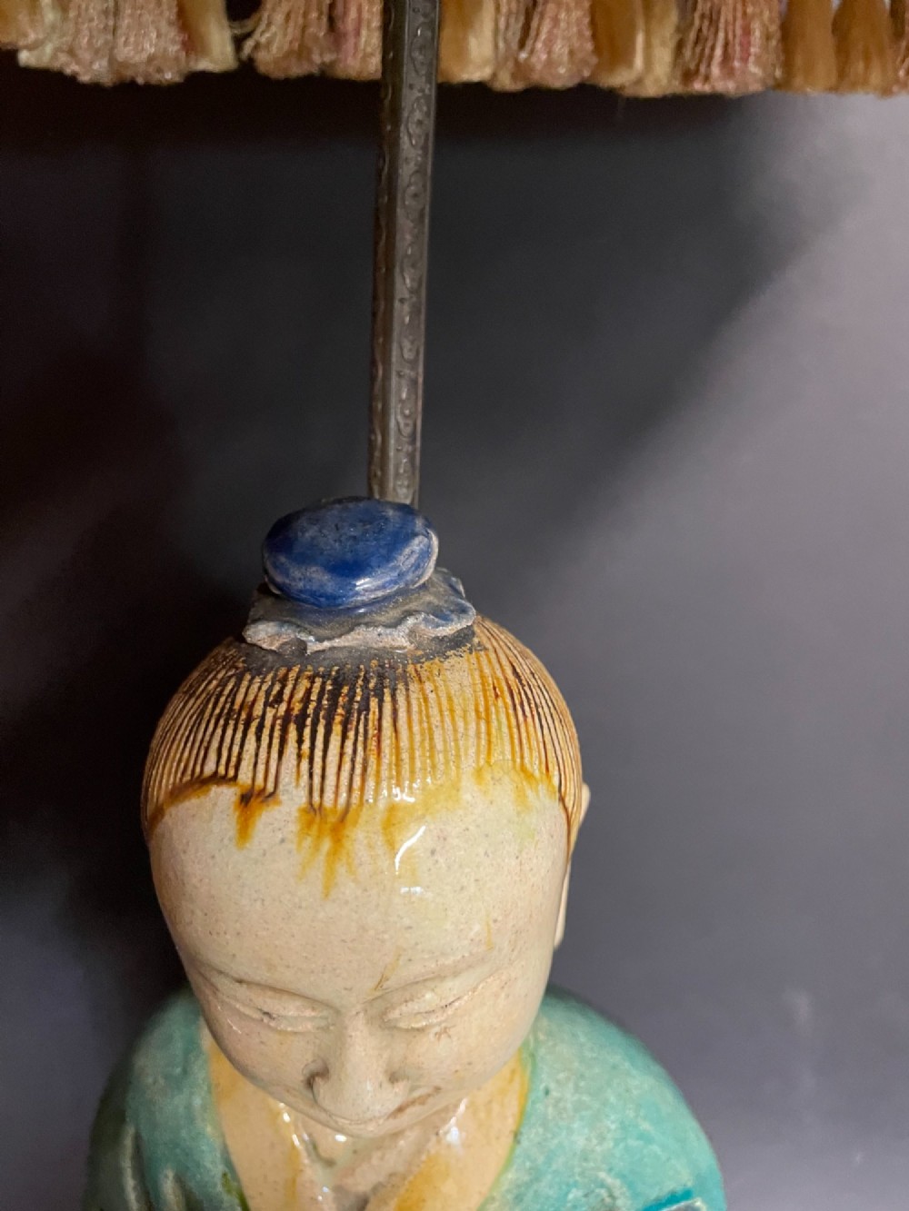 A Chinese porcelain figure table lamp featuring a green and brown glazed figurine on a black base topped with a tasseled fabric shade showing a painted landscape. View II