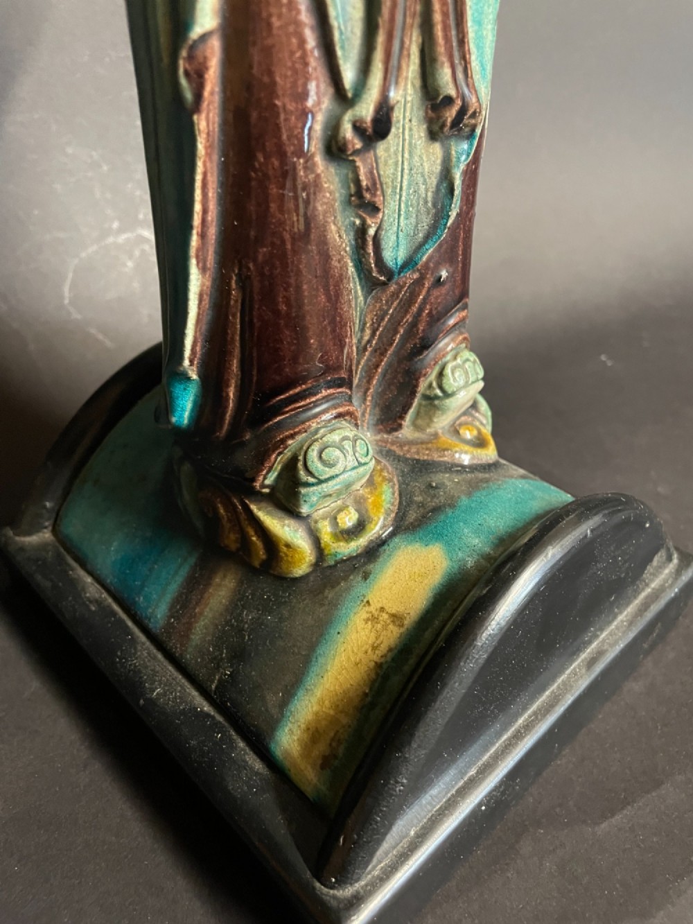 A Chinese porcelain figure table lamp featuring a green and brown glazed figurine on a black base topped with a tasseled fabric shade showing a painted landscape. View VI