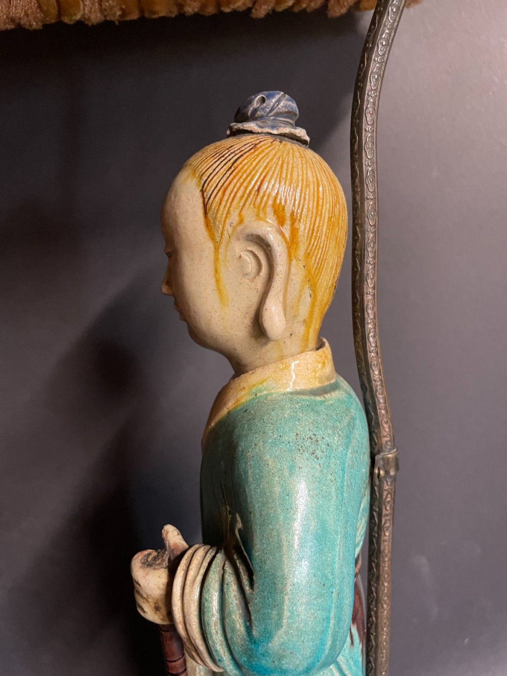 A Chinese porcelain figure table lamp featuring a green and brown glazed figurine on a black base topped with a tasseled fabric shade showing a painted landscape. View X