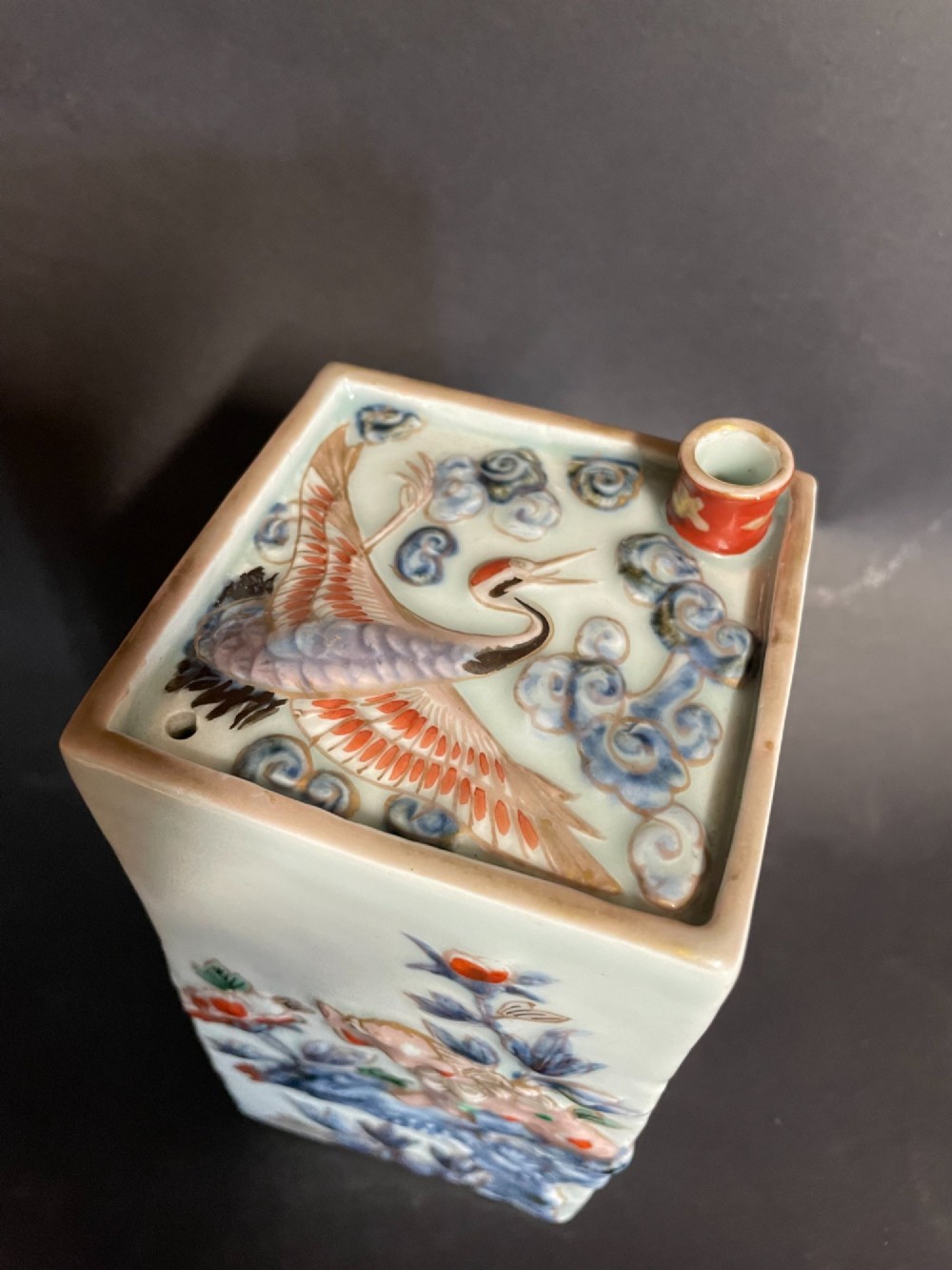 A rectangular off-white Japanese porcelain tokuri flask featuring relief carvings and hand-painted polychrome enamel depictions of a Shishi lion dog and floral foliage. View II