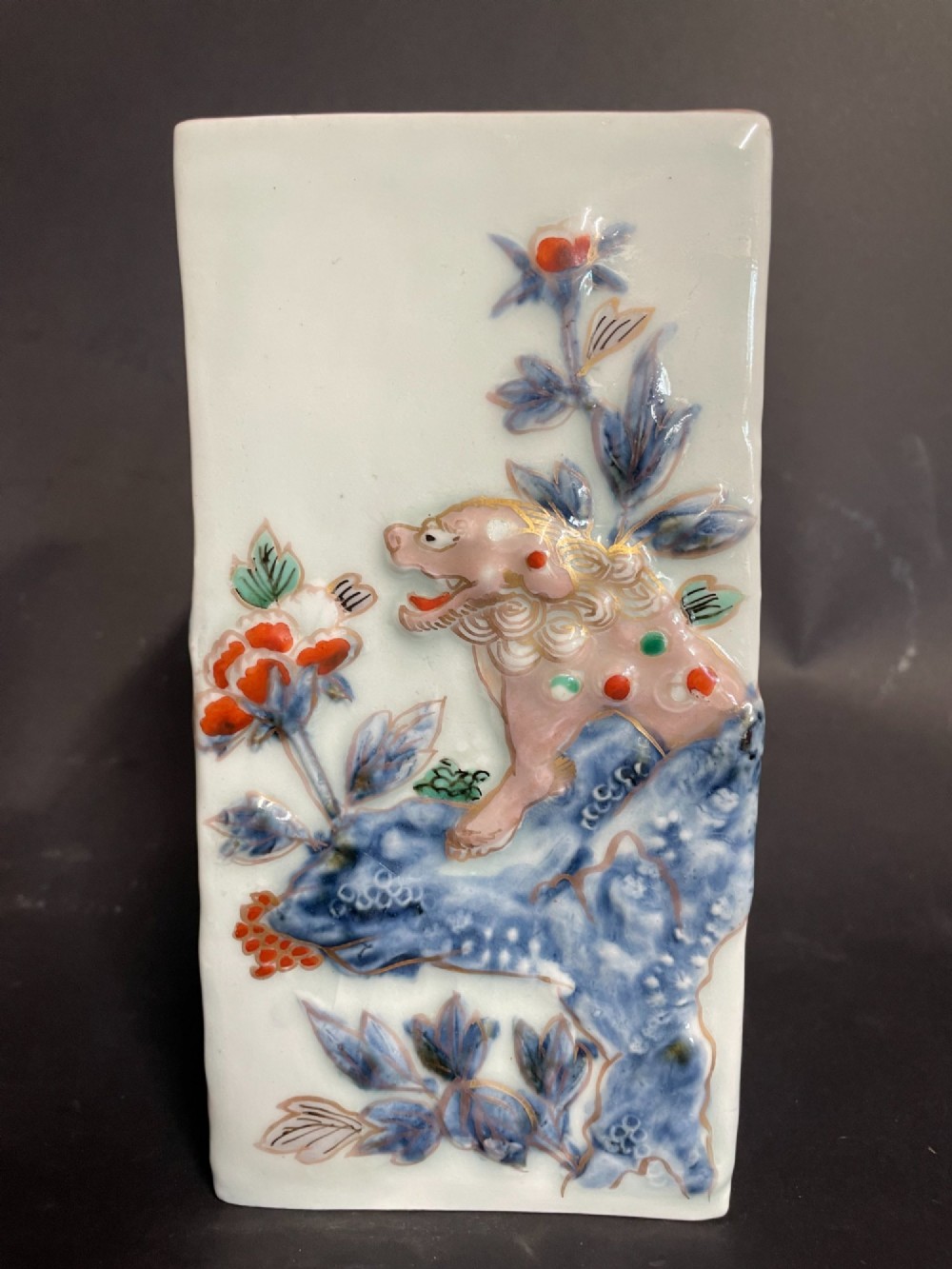 A rectangular off-white Japanese porcelain tokuri flask featuring relief carvings and hand-painted polychrome enamel depictions of a Shishi lion dog and floral foliage. View III