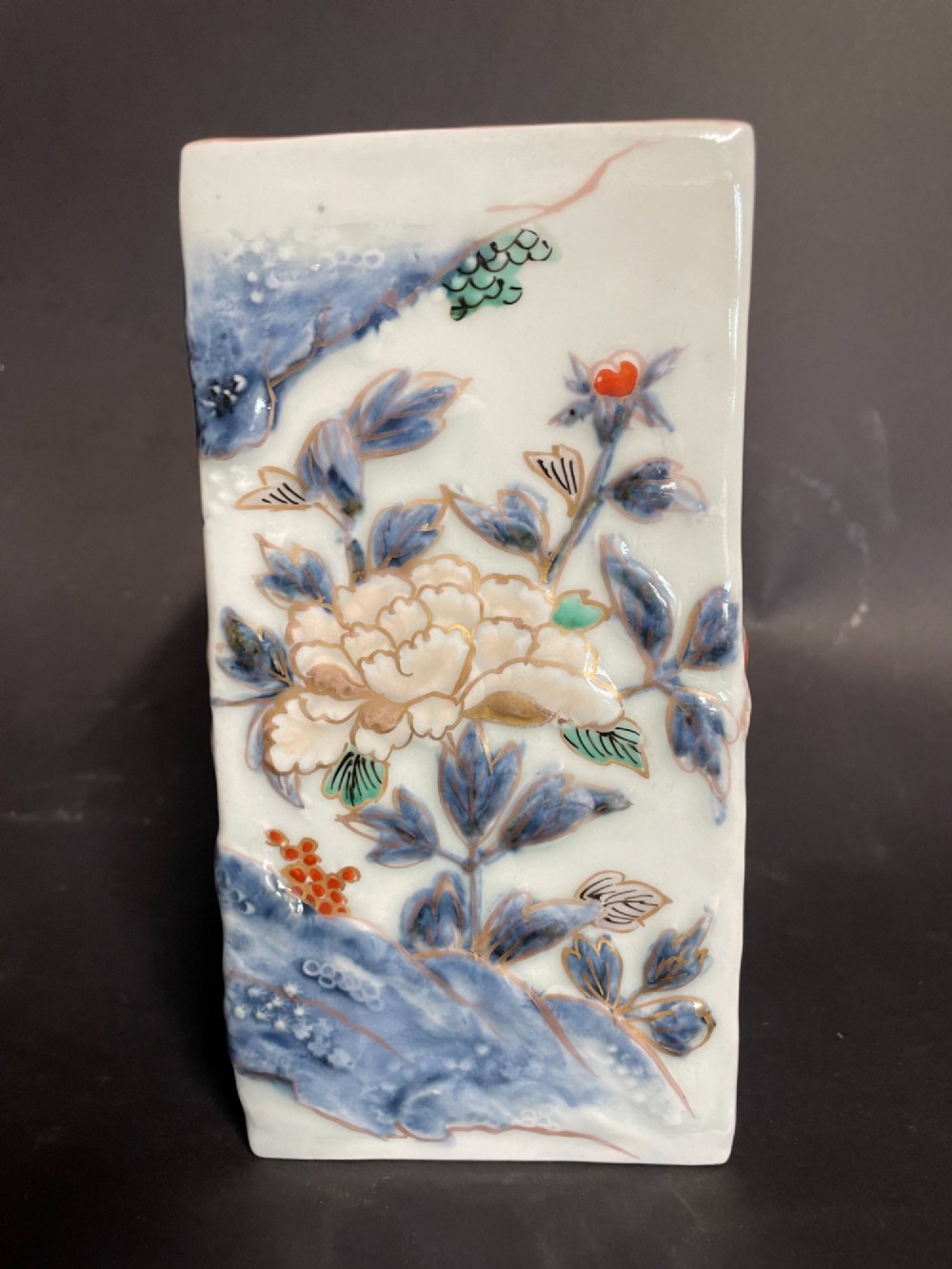 A rectangular off-white Japanese porcelain tokuri flask featuring relief carvings and hand-painted polychrome enamel depictions of a Shishi lion dog and floral foliage. View IV