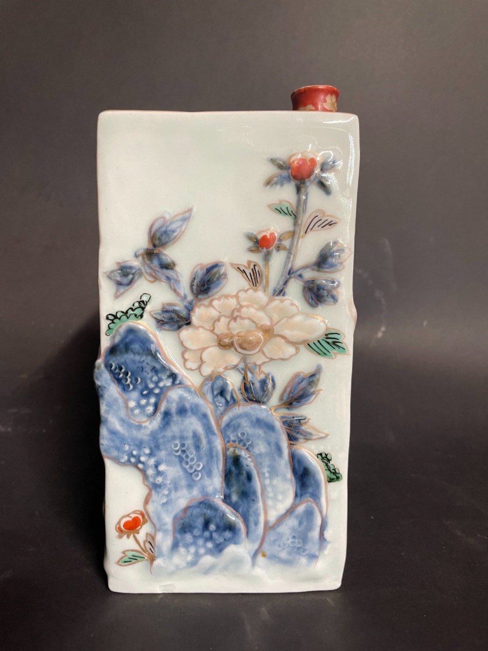 A rectangular off-white Japanese porcelain tokuri flask featuring relief carvings and hand-painted polychrome enamel depictions of a Shishi lion dog and floral foliage. View VI