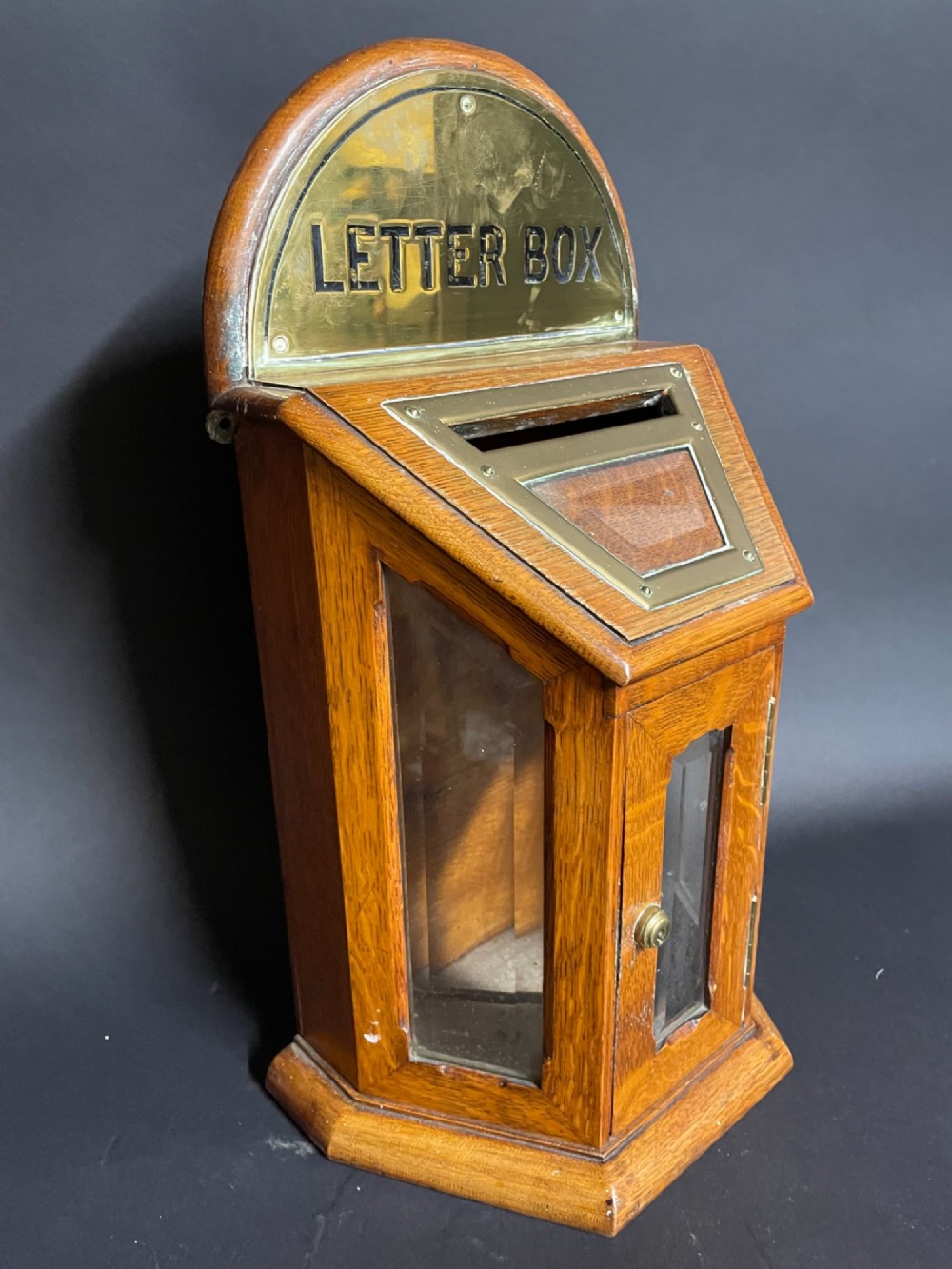 A Victorian oak tabletop letter box featuring brass fittings, a sloped aperture slot, glass side panels, and an arched brass top plate stamped LETTER BOX.
