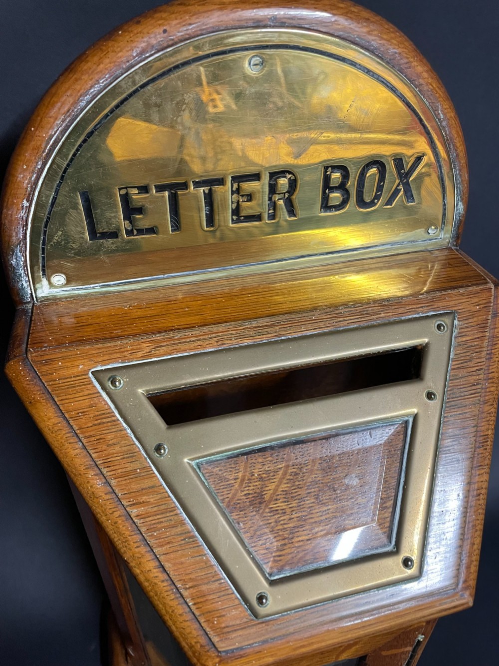 A Victorian oak tabletop letter box featuring brass fittings, a sloped aperture slot, glass side panels, and an arched brass top plate stamped LETTER BOX. View II