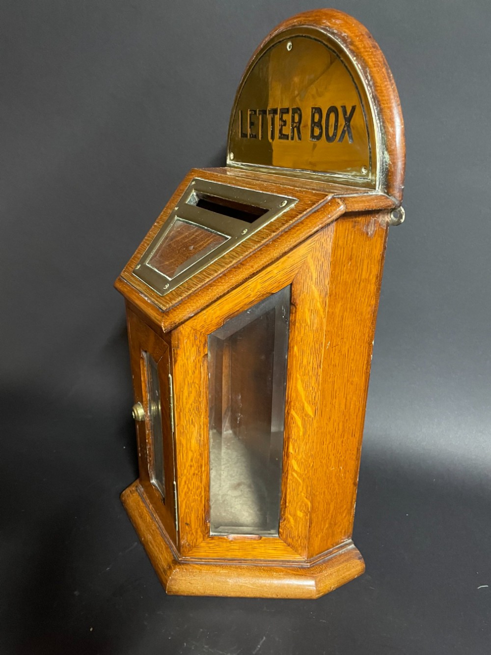 A Victorian oak tabletop letter box featuring brass fittings, a sloped aperture slot, glass side panels, and an arched brass top plate stamped LETTER BOX. View IV
