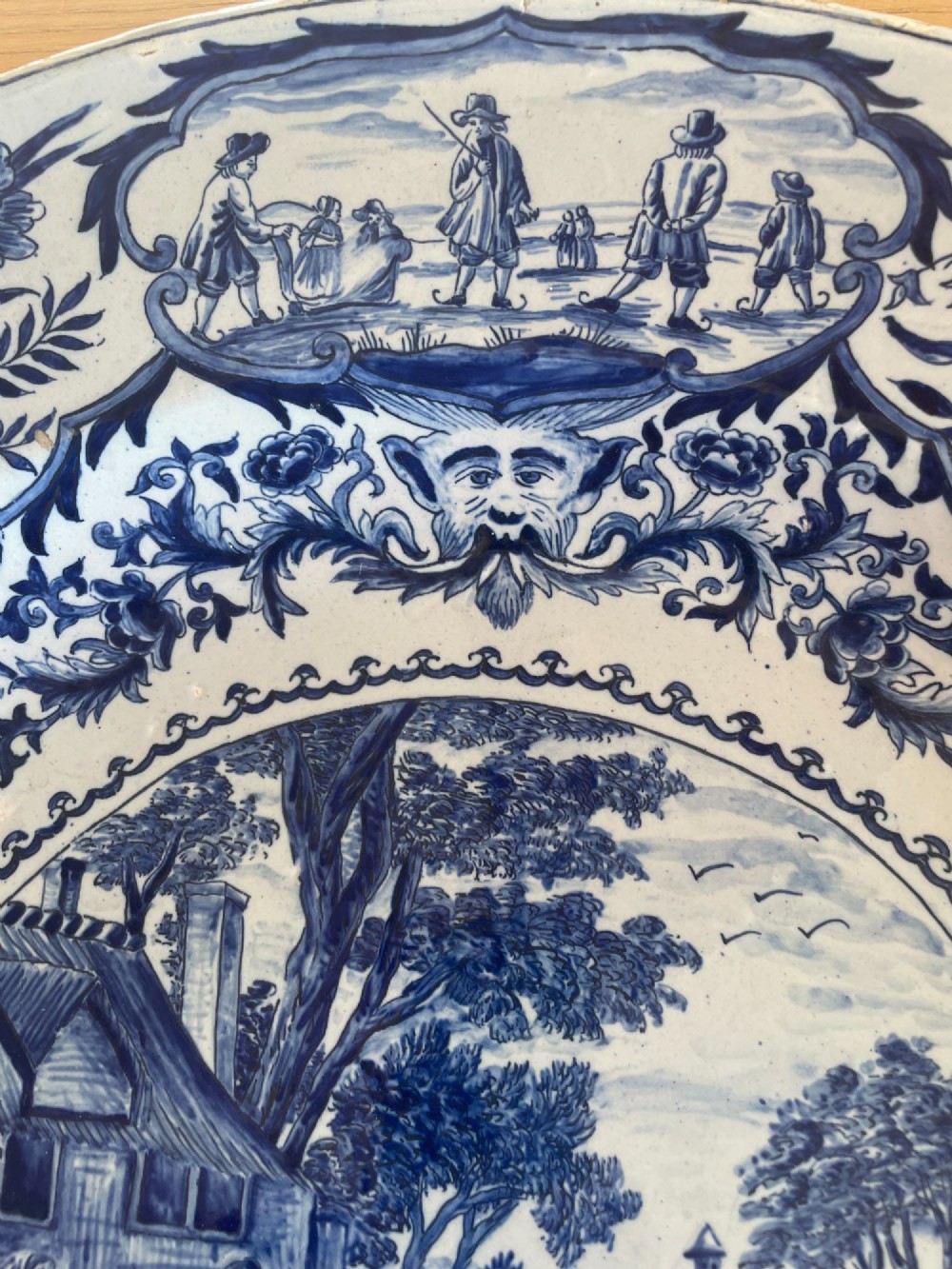 A circular Dutch Delft tin-glazed earthenware charger decorated in cobalt blue and white with a central pictorial tavern scene surrounded by ornate floral and cartouche borders. View III