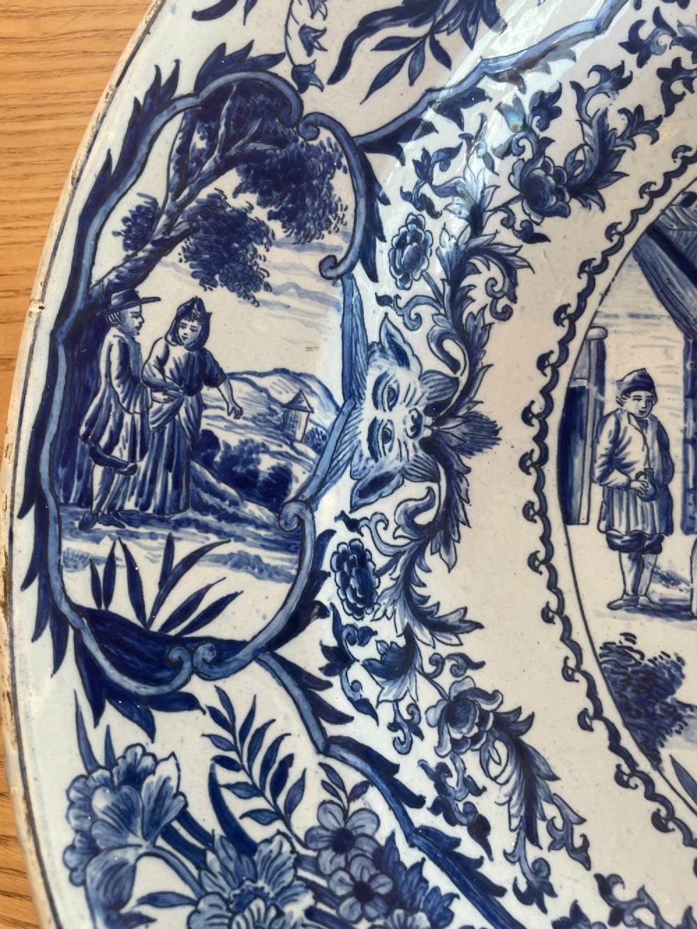 A circular Dutch Delft tin-glazed earthenware charger decorated in cobalt blue and white with a central pictorial tavern scene surrounded by ornate floral and cartouche borders. View IV