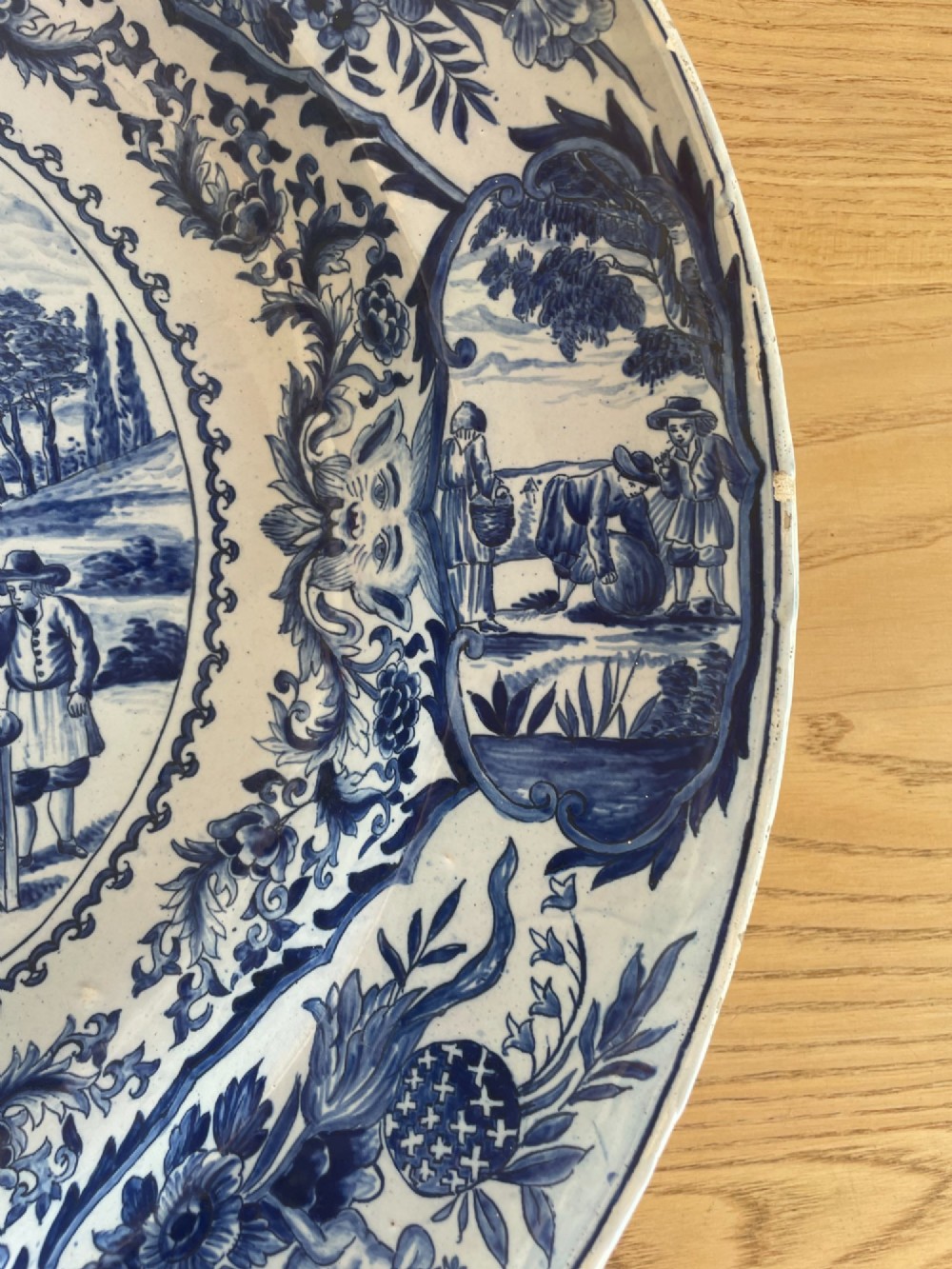 A circular Dutch Delft tin-glazed earthenware charger decorated in cobalt blue and white with a central pictorial tavern scene surrounded by ornate floral and cartouche borders. View VI