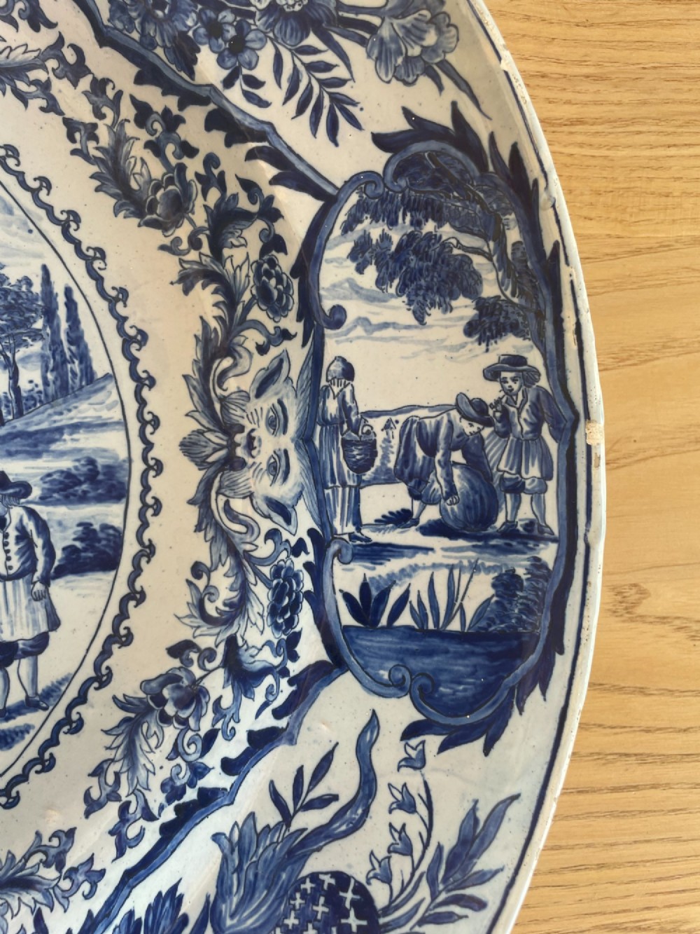 A circular Dutch Delft tin-glazed earthenware charger decorated in cobalt blue and white with a central pictorial tavern scene surrounded by ornate floral and cartouche borders. View VII