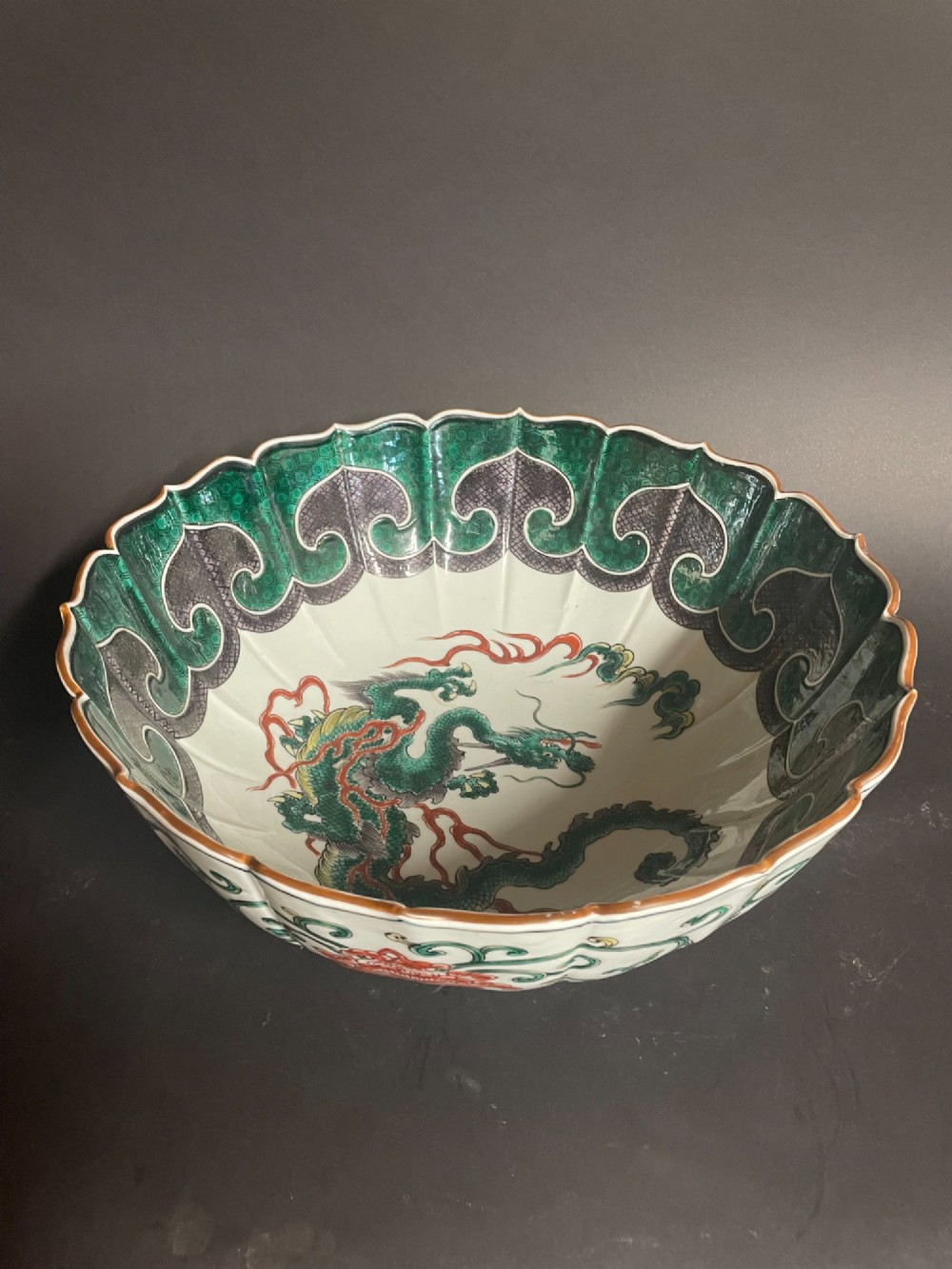 A fluted Japanese porcelain bowl with a scalloped edge, decorated with a central painted green dragon and ornate enamel borders.
