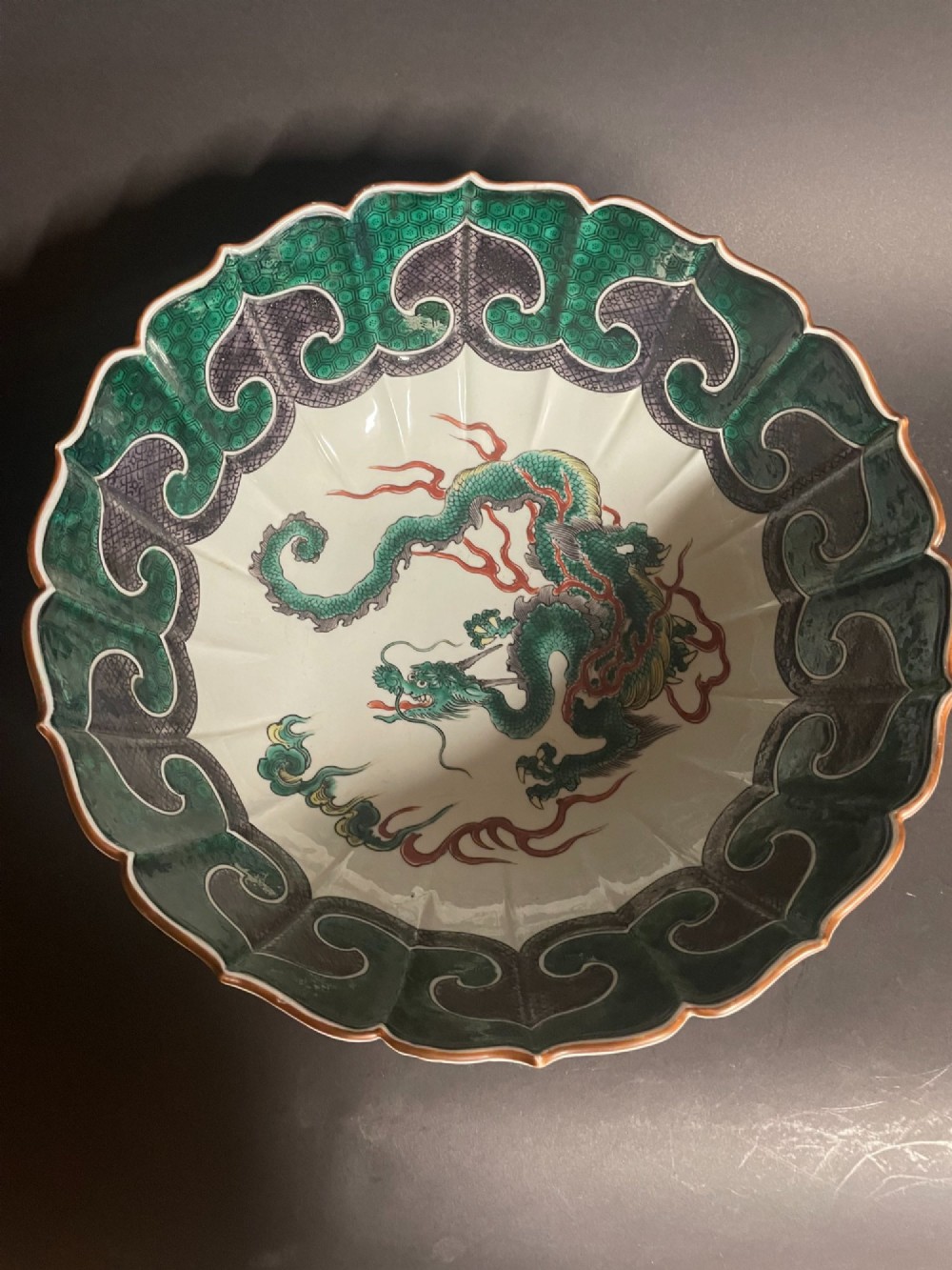 A fluted Japanese porcelain bowl with a scalloped edge, decorated with a central painted green dragon and ornate enamel borders. View II