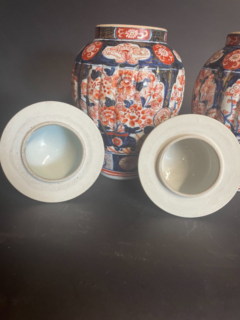 A pair of ribbed porcelain lidded jars decorated in a Japanese Imari pattern of cobalt blue, iron red, and gilt floral motifs with domed covers. View V