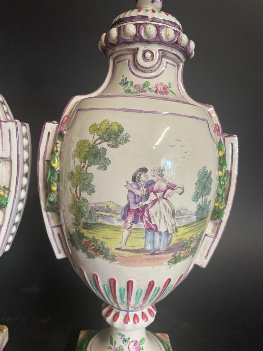 A pair of antique French Sceaux faience lidded urns decorated with hand-painted pastoral scenes, floral garlands, and moulding on square bases. View II