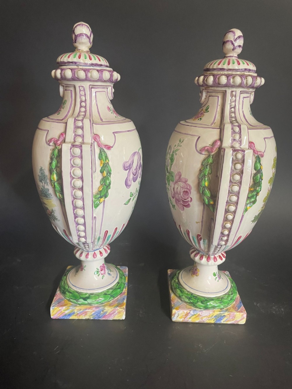 A pair of antique French Sceaux faience lidded urns decorated with hand-painted pastoral scenes, floral garlands, and moulding on square bases. View V