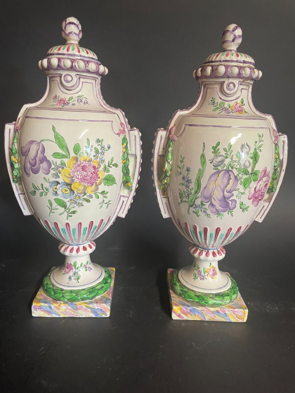 A pair of antique French Sceaux faience lidded urns decorated with hand-painted pastoral scenes, floral garlands, and moulding on square bases. View VI