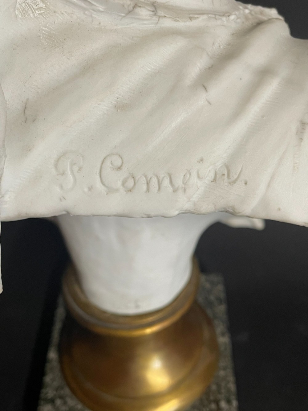 A white carved bust of a woman with draped classical clothing, mounted on a turned gold-tone socle and a square speckled granite base. View VII