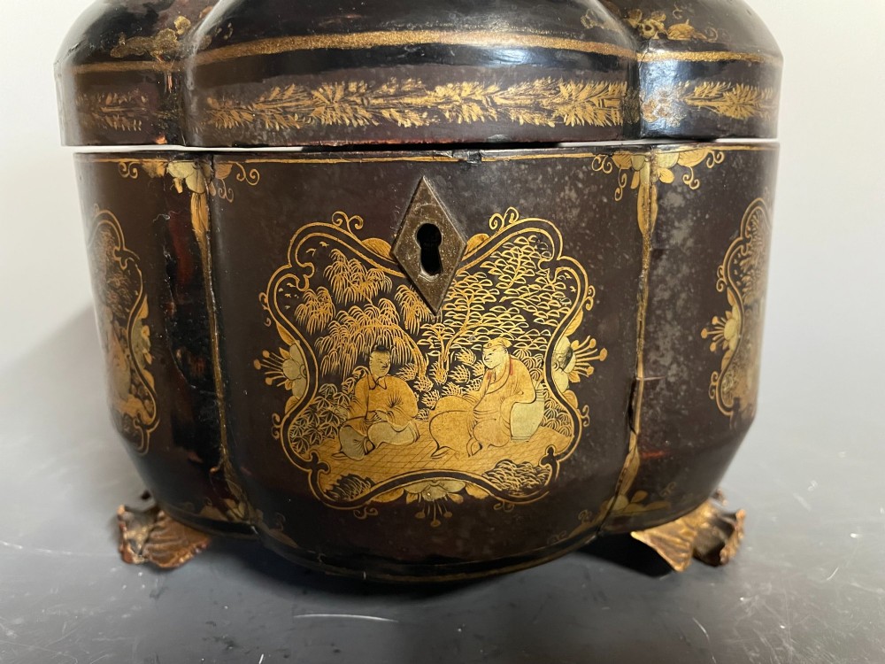 A lobed black lacquer Chinese export tea caddy decorated with gold painted figural scenes, featuring a brass escutcheon and carved feet. View II