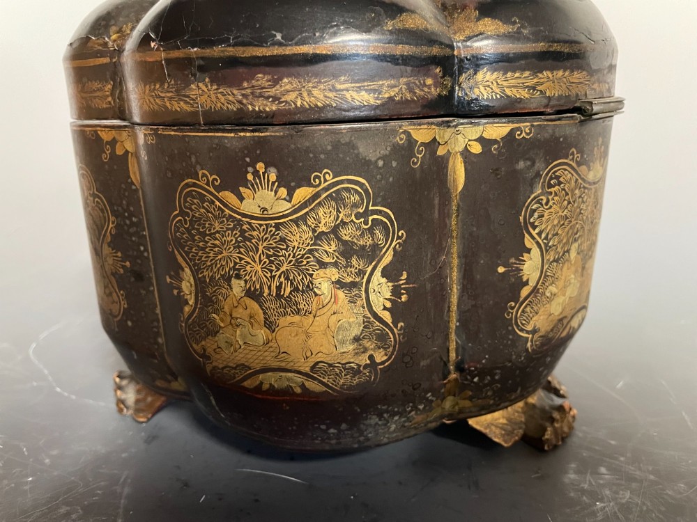 A lobed black lacquer Chinese export tea caddy decorated with gold painted figural scenes, featuring a brass escutcheon and carved feet. View V