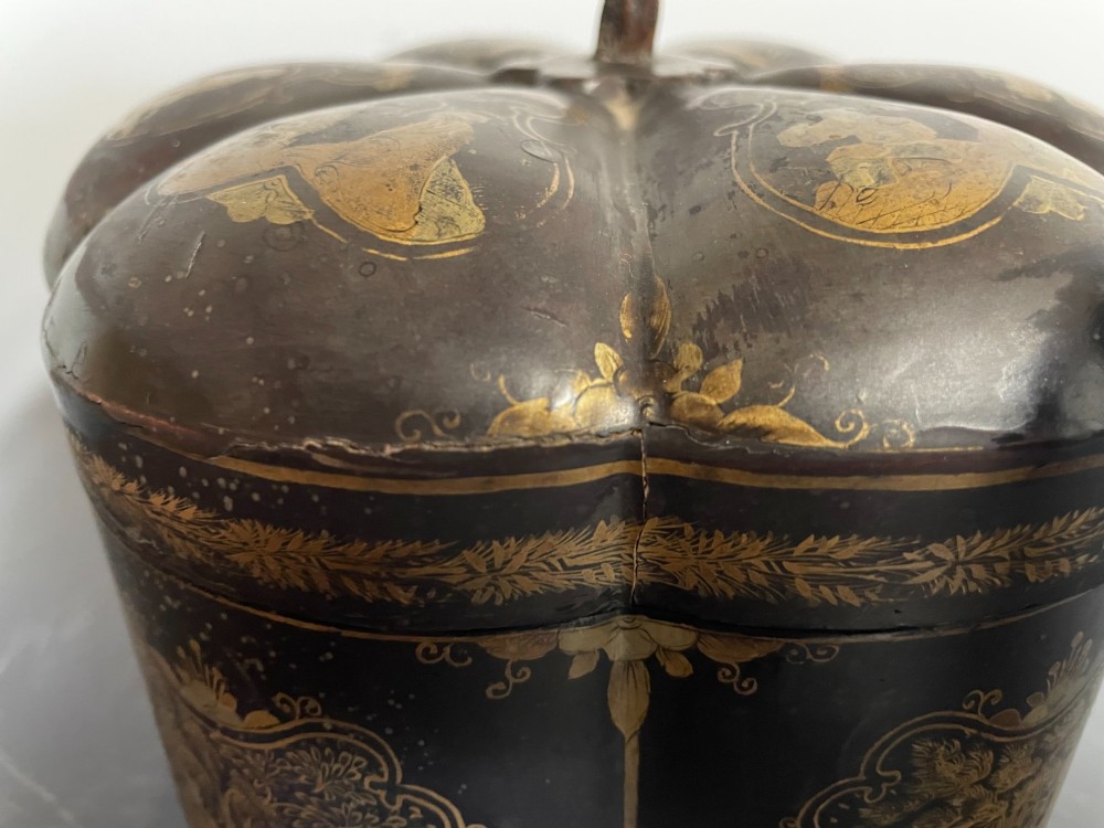 A lobed black lacquer Chinese export tea caddy decorated with gold painted figural scenes, featuring a brass escutcheon and carved feet. View VIII