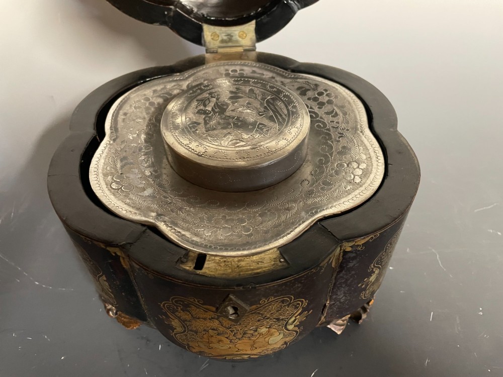 A lobed black lacquer Chinese export tea caddy decorated with gold painted figural scenes, featuring a brass escutcheon and carved feet. View X