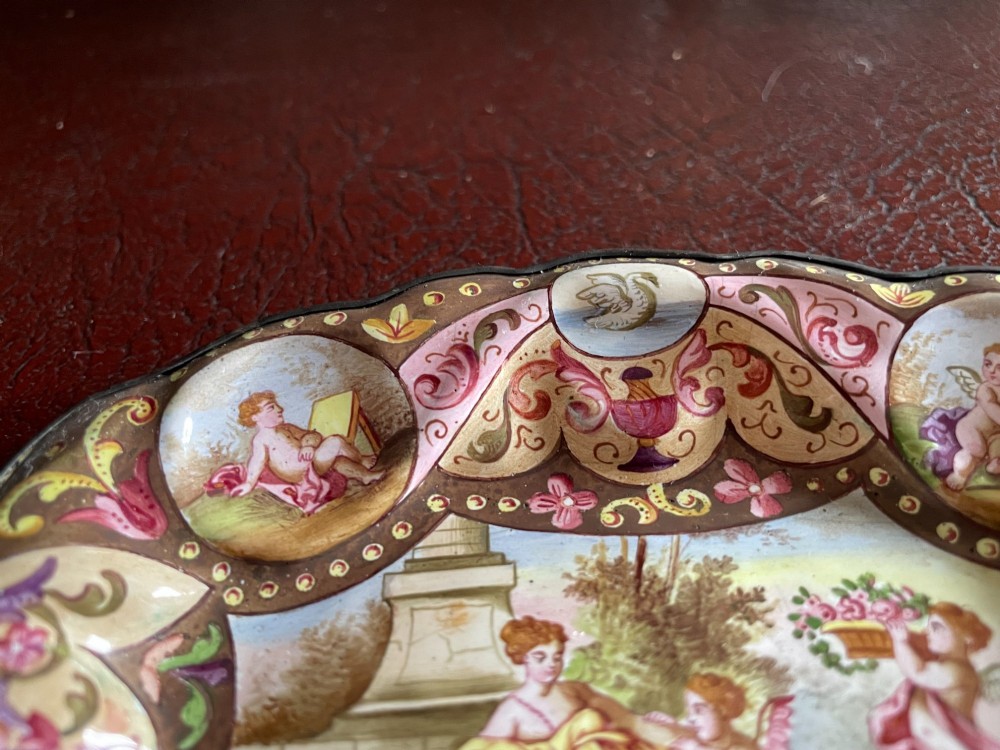 An oval enamelled dish with lobed edges, featuring hand-painted classical figures in the centre surrounded by cherub portraits and scrollwork along the border. View II