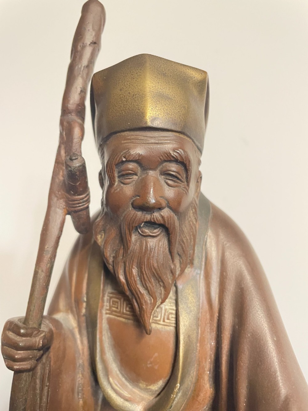 A patinated cast bronze Japanese figure depicting a bearded scholar wearing traditional robes and a tall headpiece while holding a walking staff. View II