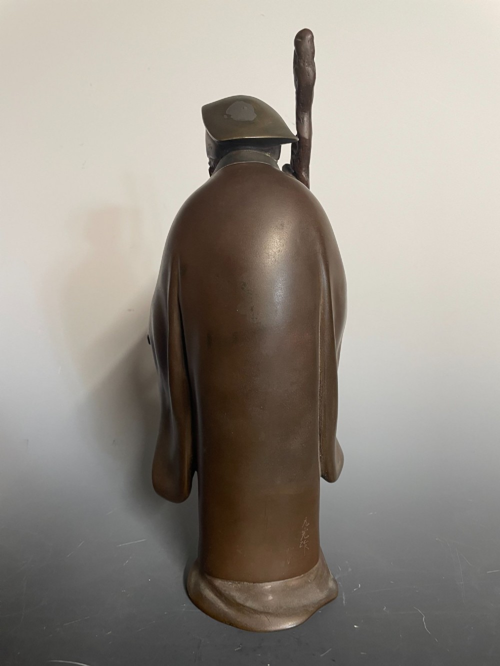 A patinated cast bronze Japanese figure depicting a bearded scholar wearing traditional robes and a tall headpiece while holding a walking staff. View IV