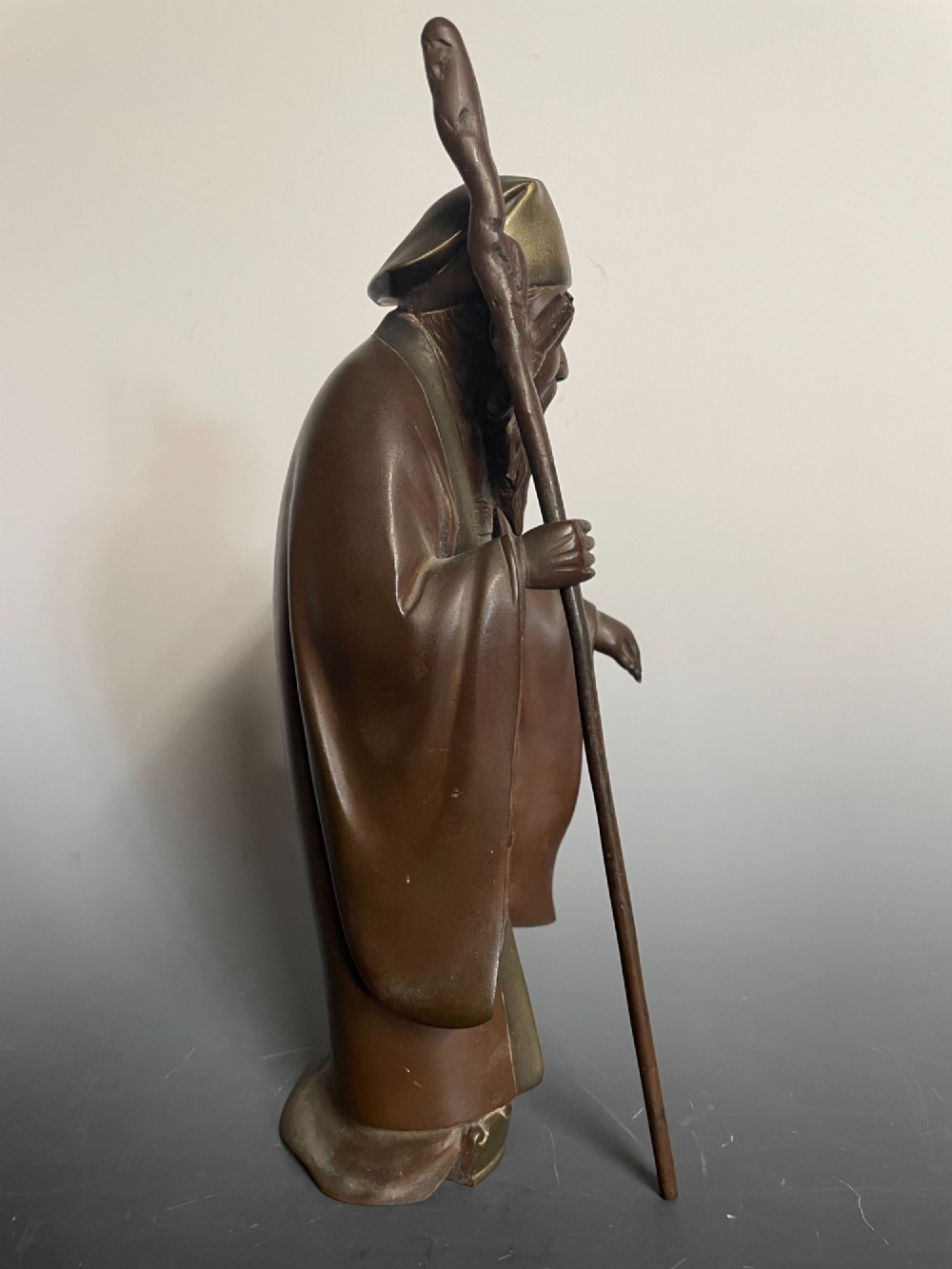 A patinated cast bronze Japanese figure depicting a bearded scholar wearing traditional robes and a tall headpiece while holding a walking staff. View V