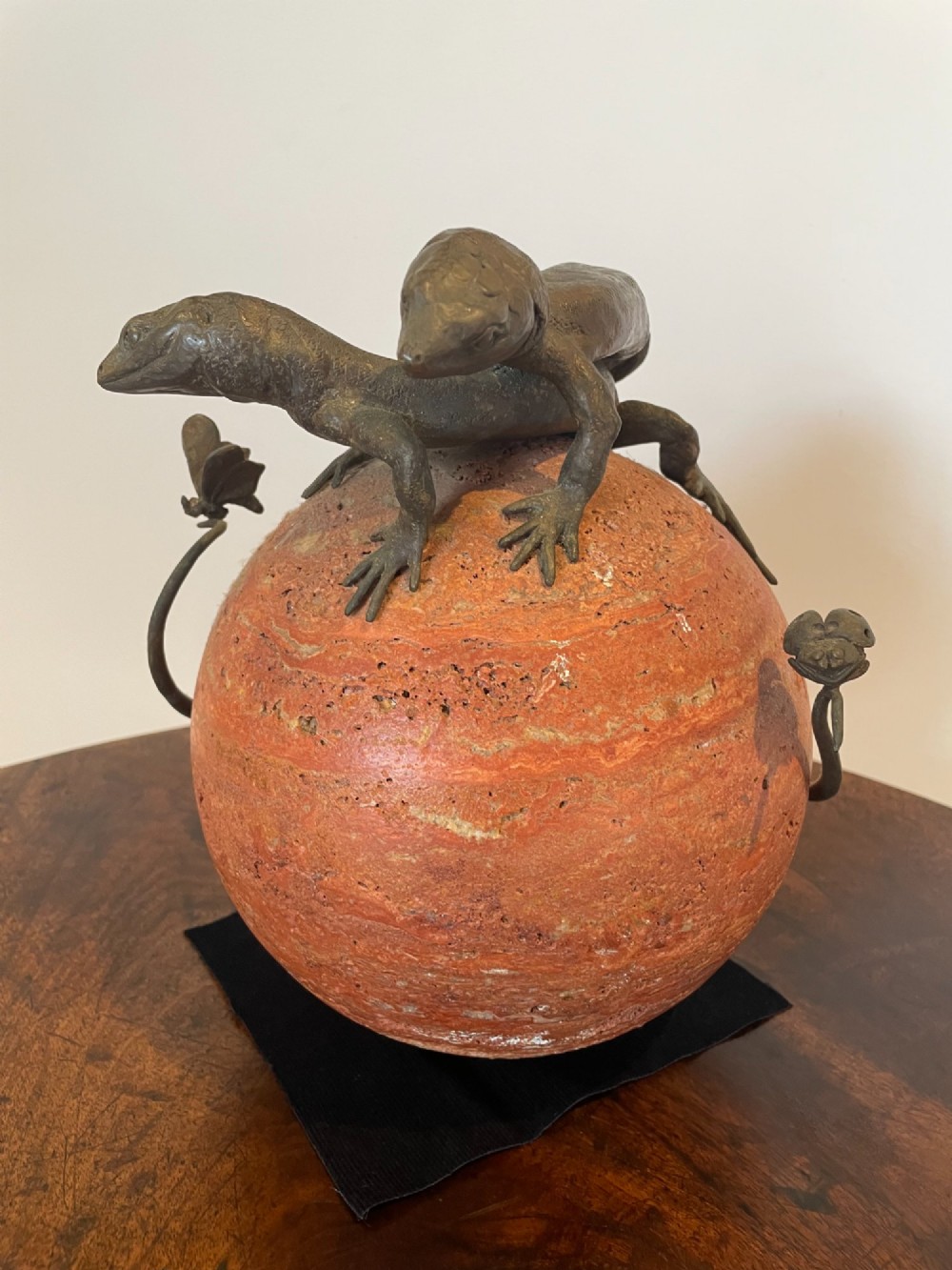 A dark bronze sculpture depicting two realistic lizards perched on top of a spherical red veined marble base. View II