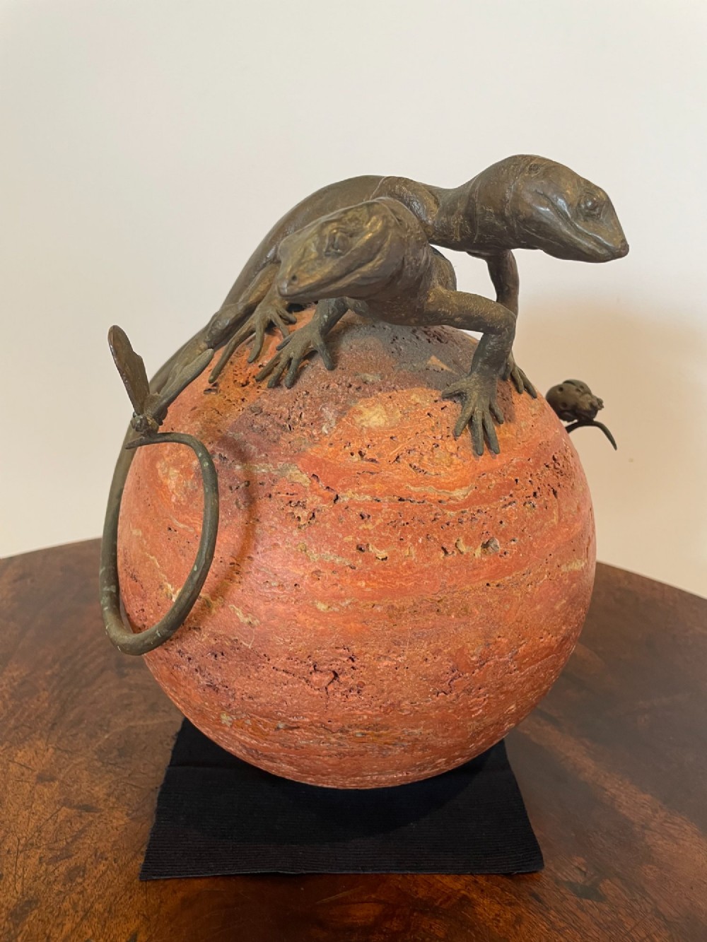 A dark bronze sculpture depicting two realistic lizards perched on top of a spherical red veined marble base. View III