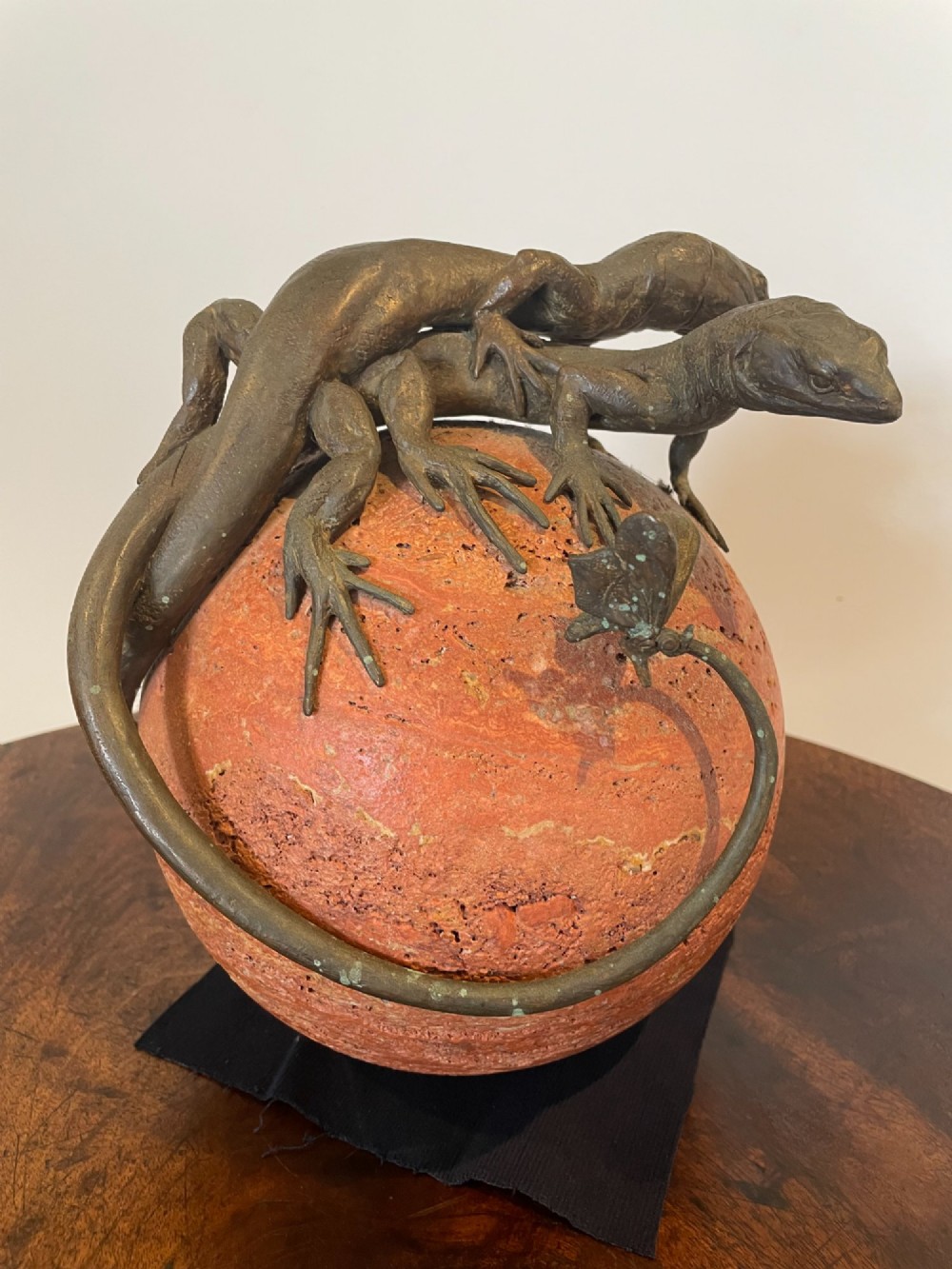 A dark bronze sculpture depicting two realistic lizards perched on top of a spherical red veined marble base. View IV