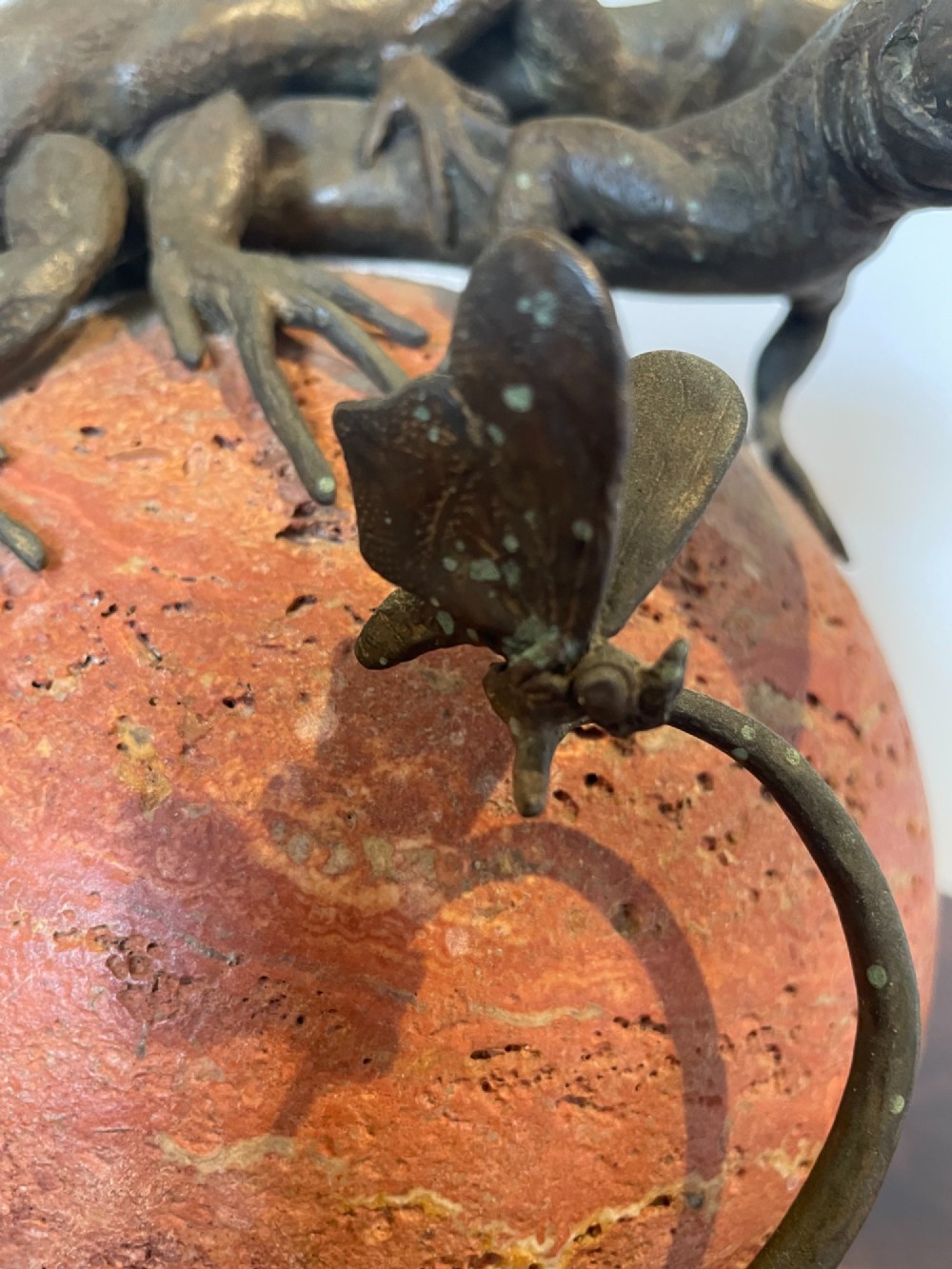 A dark bronze sculpture depicting two realistic lizards perched on top of a spherical red veined marble base. View V