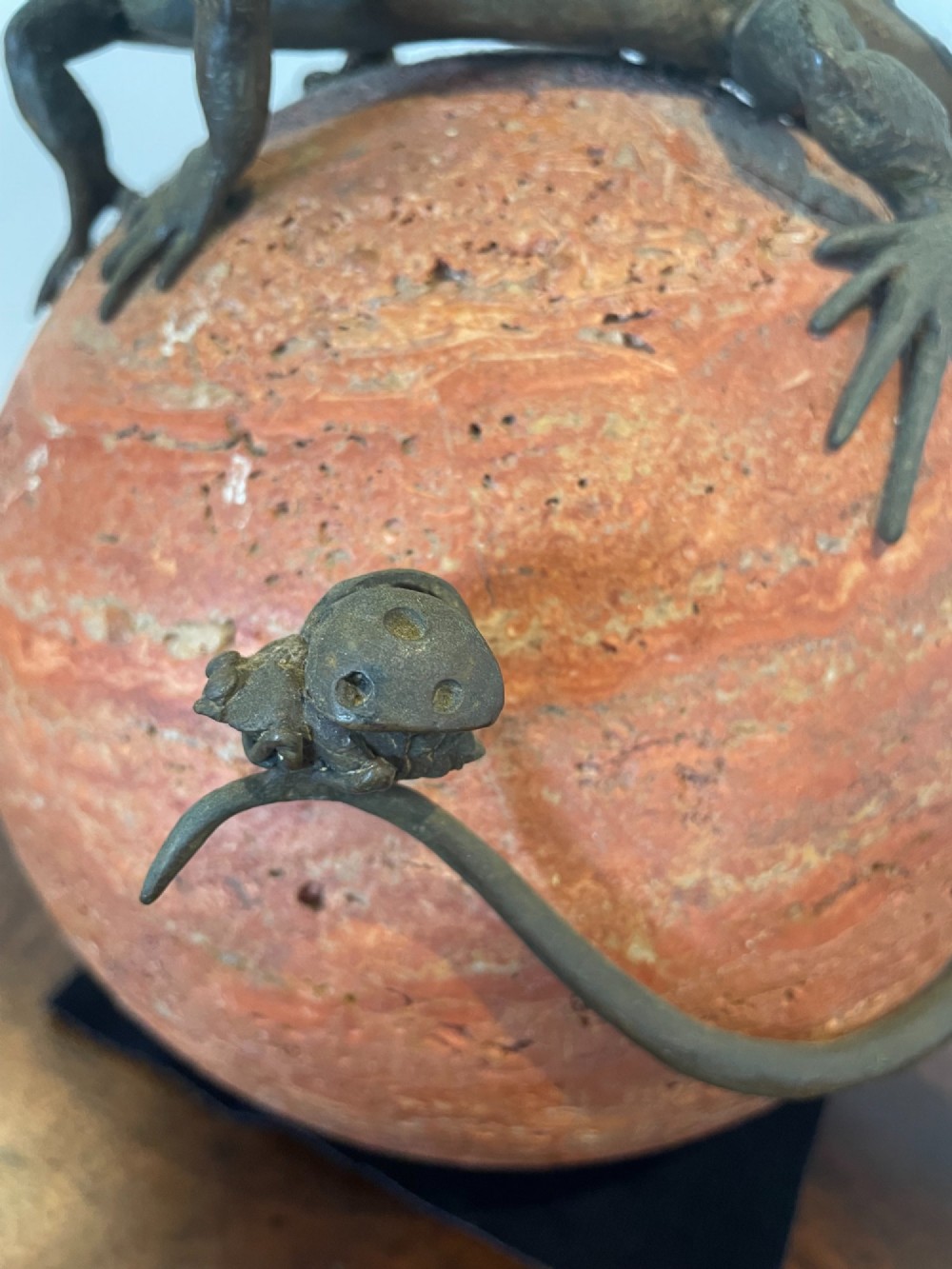 A dark bronze sculpture depicting two realistic lizards perched on top of a spherical red veined marble base. View VI