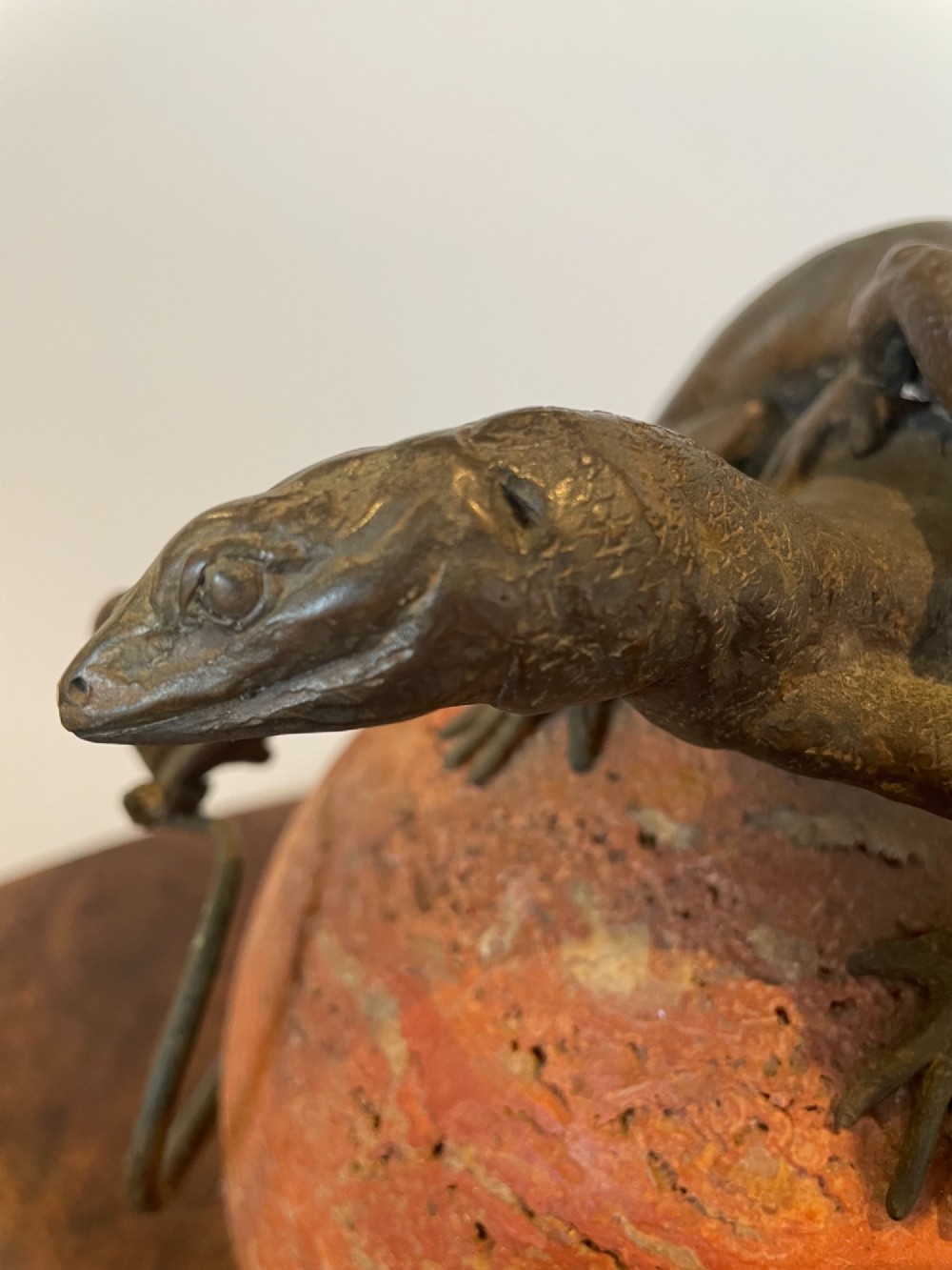 A dark bronze sculpture depicting two realistic lizards perched on top of a spherical red veined marble base. View VII