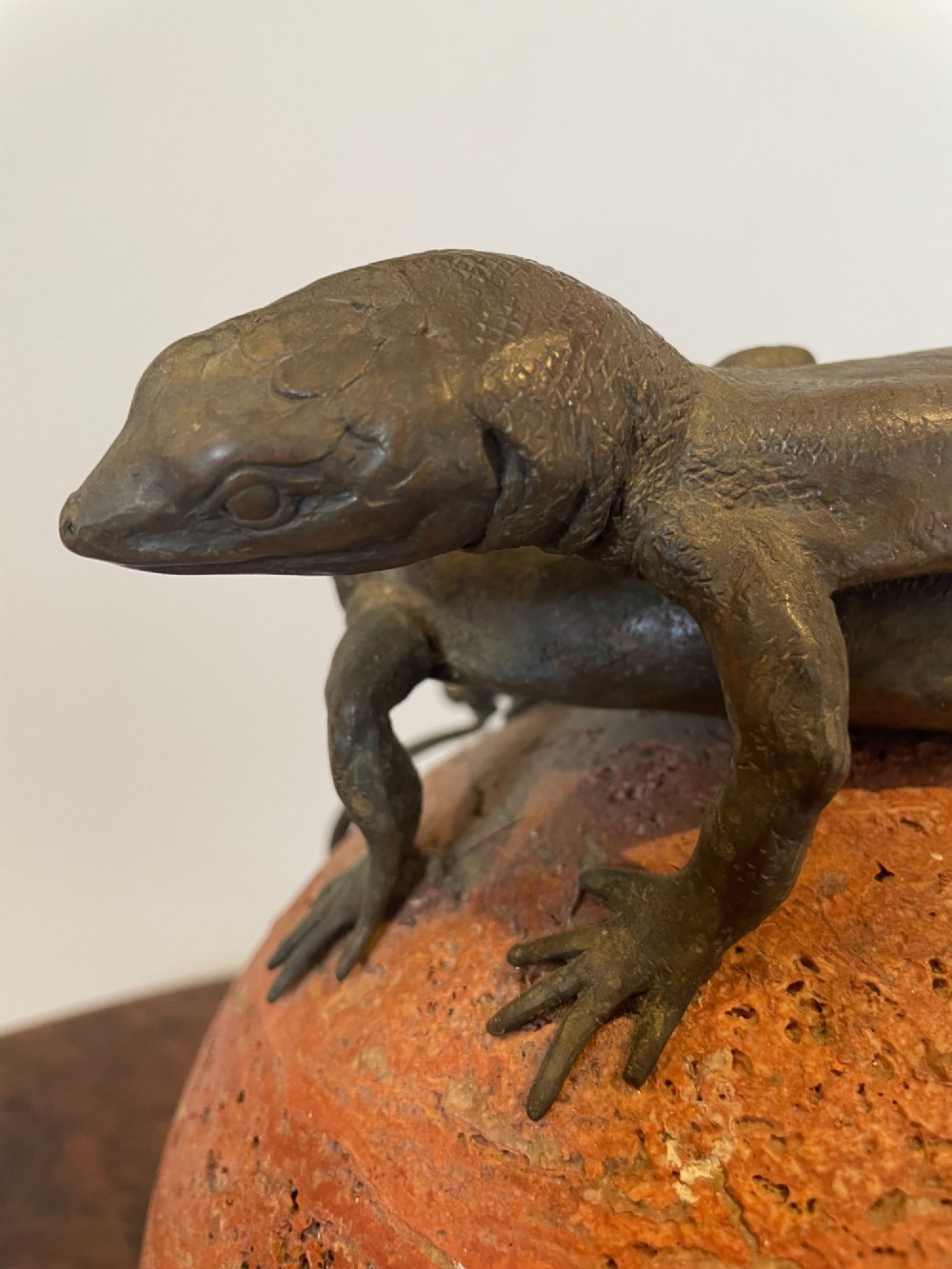 A dark bronze sculpture depicting two realistic lizards perched on top of a spherical red veined marble base. View VIII
