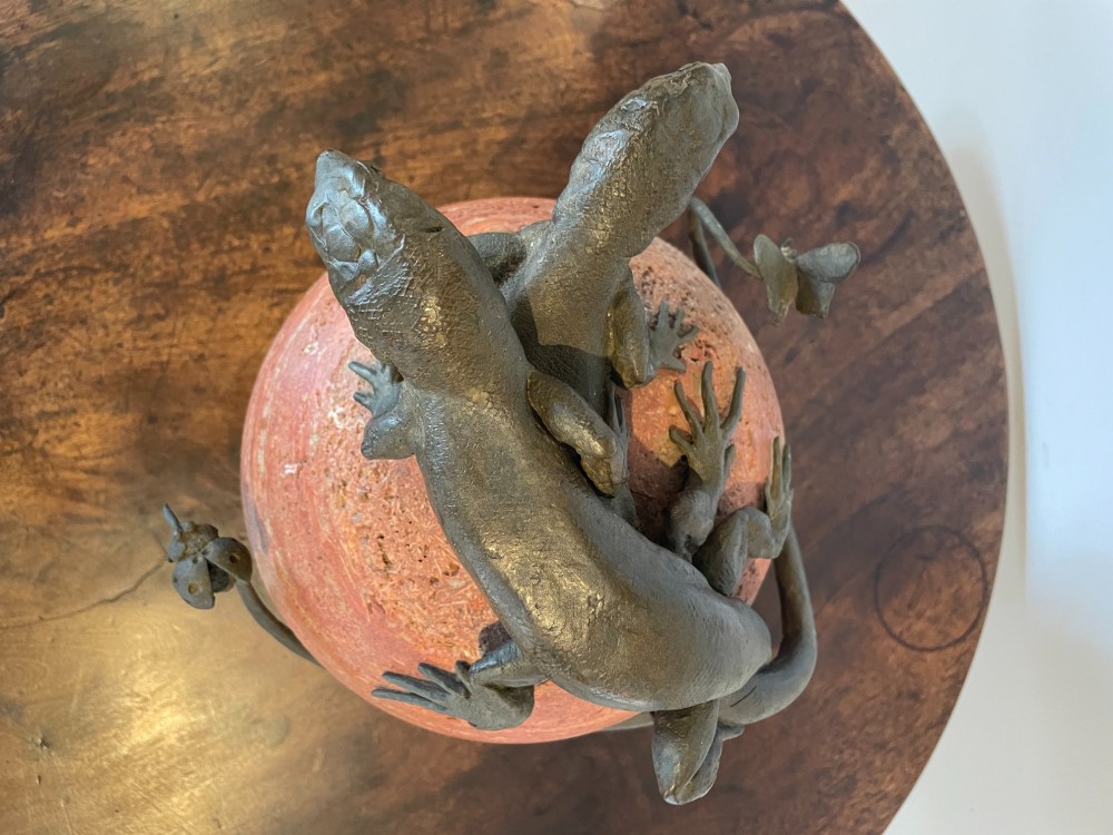A dark bronze sculpture depicting two realistic lizards perched on top of a spherical red veined marble base. View IX